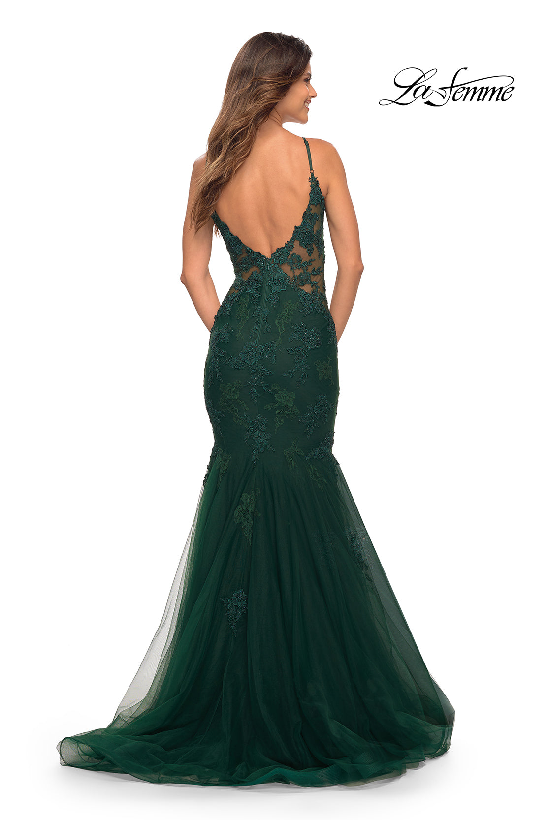 A woman stands with her back to the camera, wearing the La Femme Embroidered-Lace Long Mermaid Prom Dress featuring a dark green hue, sheer lace bodice, and low back. The