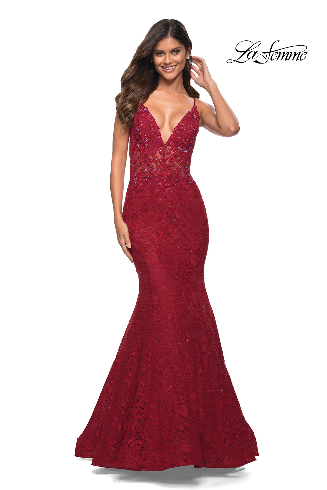 A woman wears the La Femme Lace Sheer-Waist Long Mermaid Prom Dress, a sleeveless, deep V-neck, floor-length red gown with a fitted silhouette and flared floral lace hem. The
