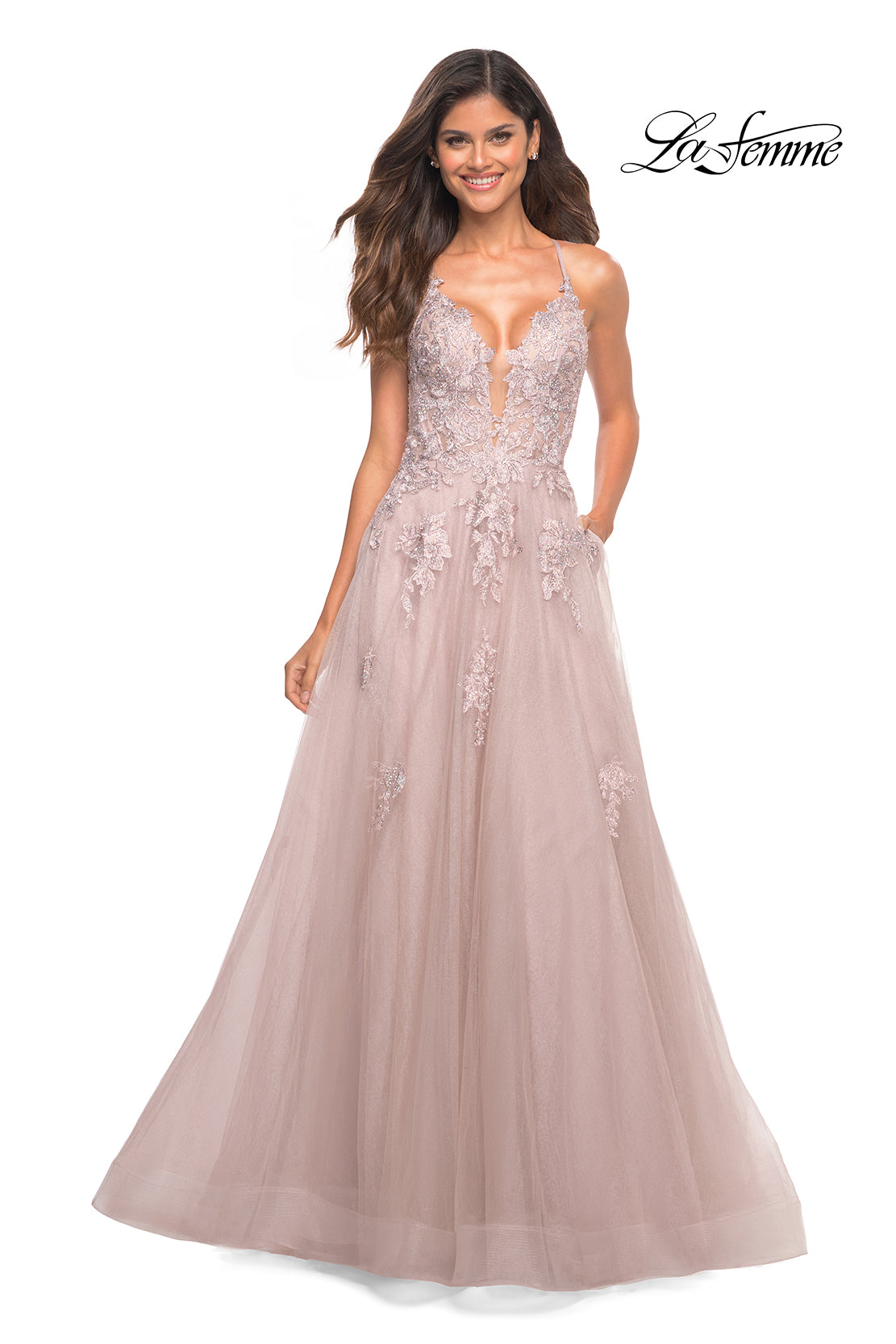 A smiling woman wears the La Femme Open-Back Long Ball Gown with Lace in blush pink, featuring a deep V neckline, thin straps, and delicate lace embroidery. The