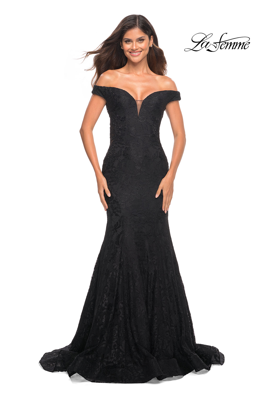 A woman stands and smiles against a plain white background, wearing the La Femme Off-the-Shoulder Long Lace Prom Dress—a fitted, black floor-length gown with a flared hem. The