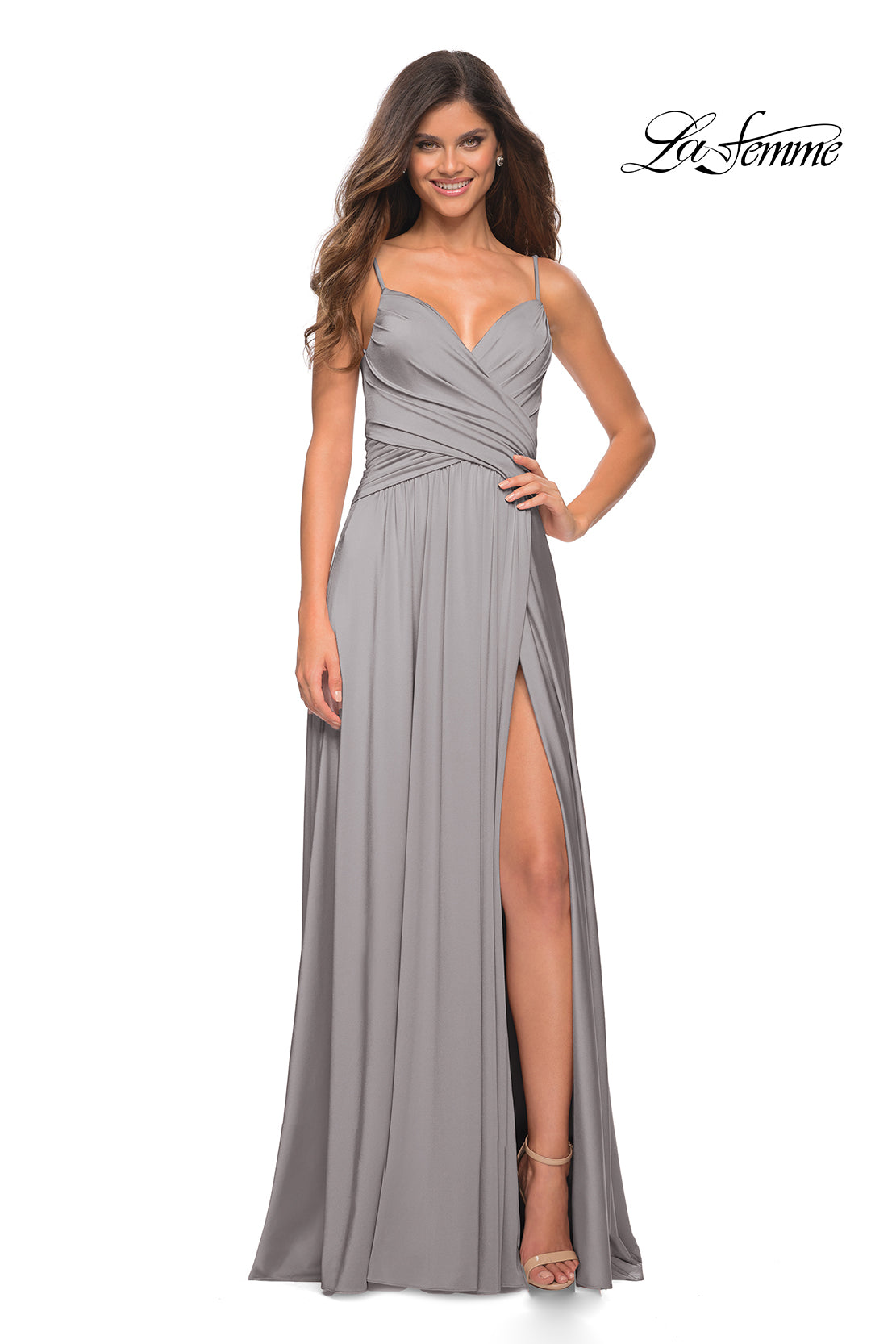 A woman wears the La Femme Simple Elegant Long Formal Prom Dress—a light gray, sleeveless A-line gown with a V-neckline, ruched bodice, thin straps, and thigh-high slit—paired with heels.