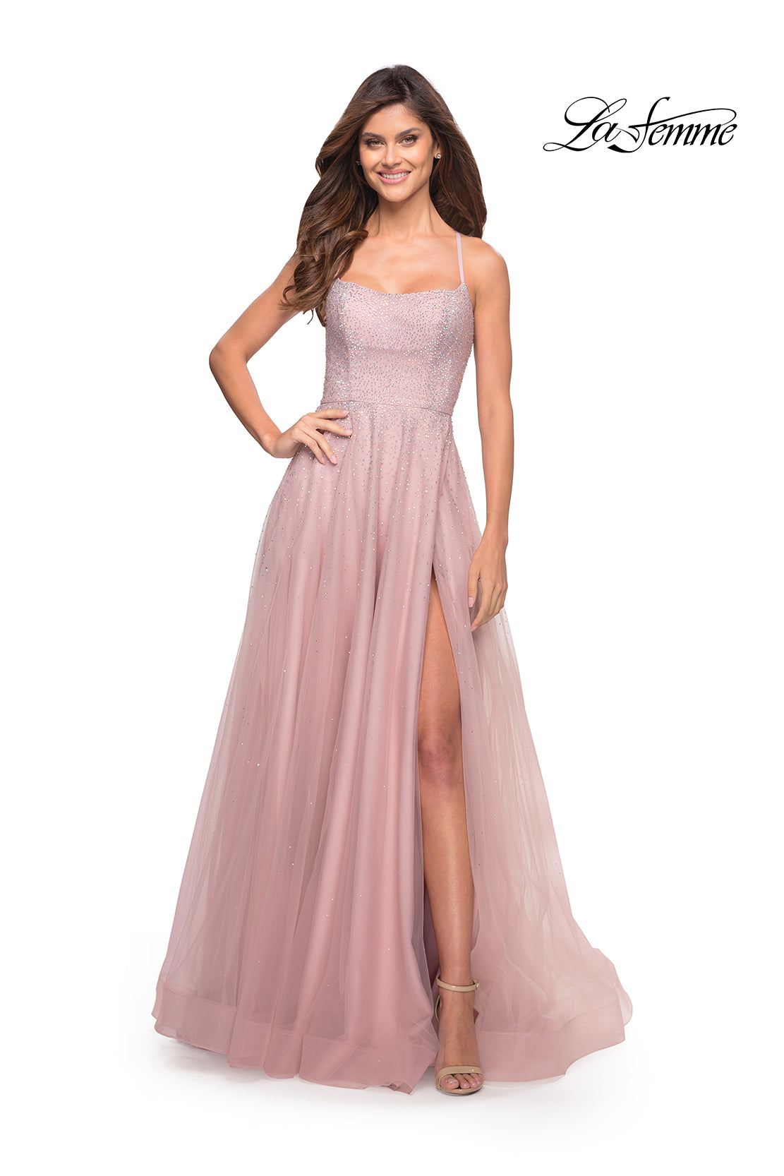 A woman wears the Corset-Back Long La Femme A-Line Prom Dress, a light pink floor-length gown with thin straps, a fitted bodice, and a high slit, as she smiles against a white background.