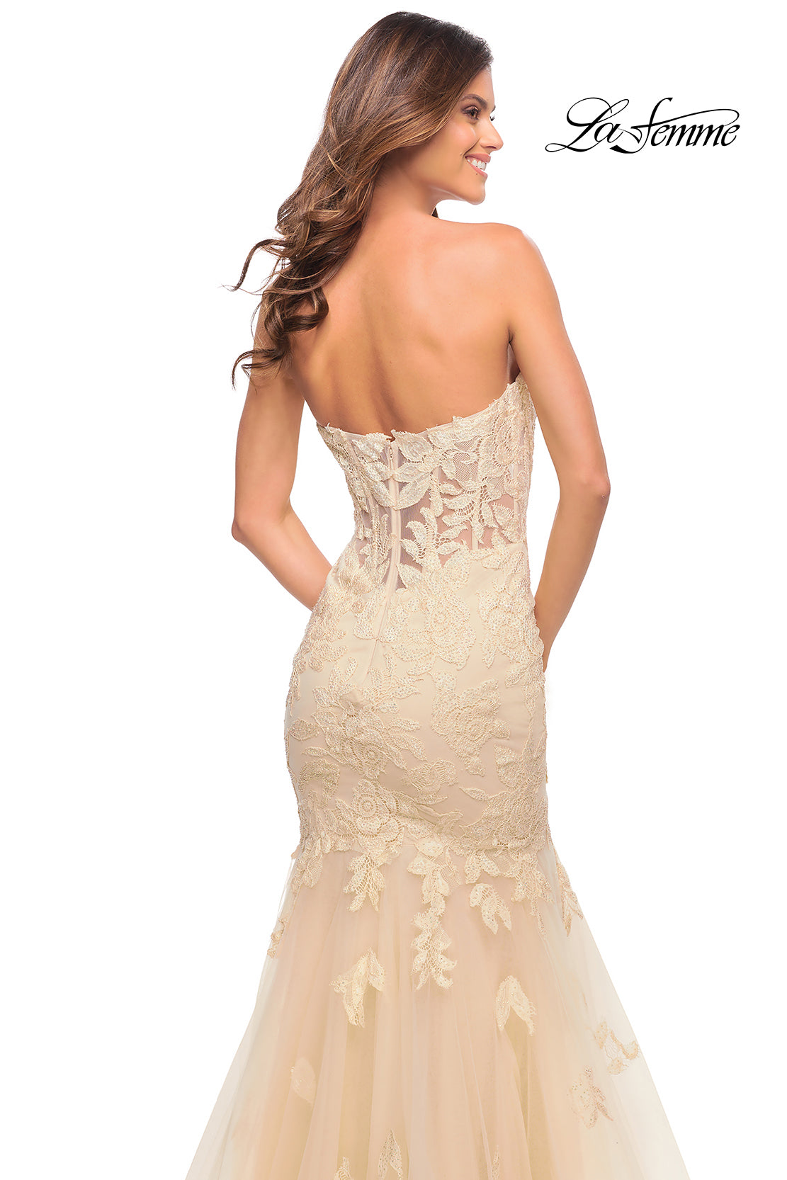 A woman models the Sheer-Back La Femme Strapless Mermaid Prom Dress in ivory lace with floral embroidery, sheer detailing, and a corset back. Photo is taken from behind; La Femme logo appears in the top right corner.