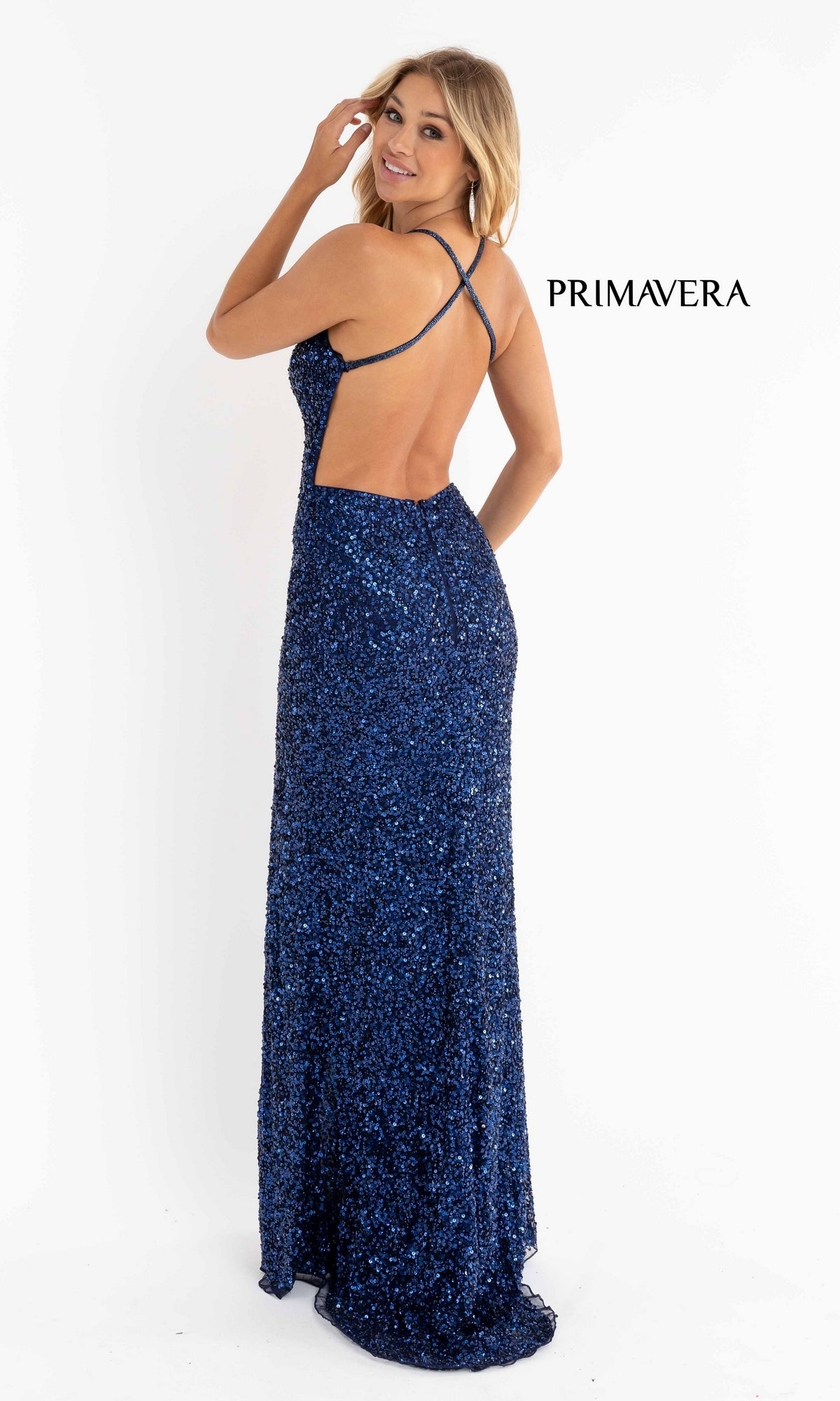 A woman in the Backless Tight Long Sequin Prom Dress 3291D stands looking over her shoulder. The dark blue gown features crisscross straps, an open back, and dazzling sequins.