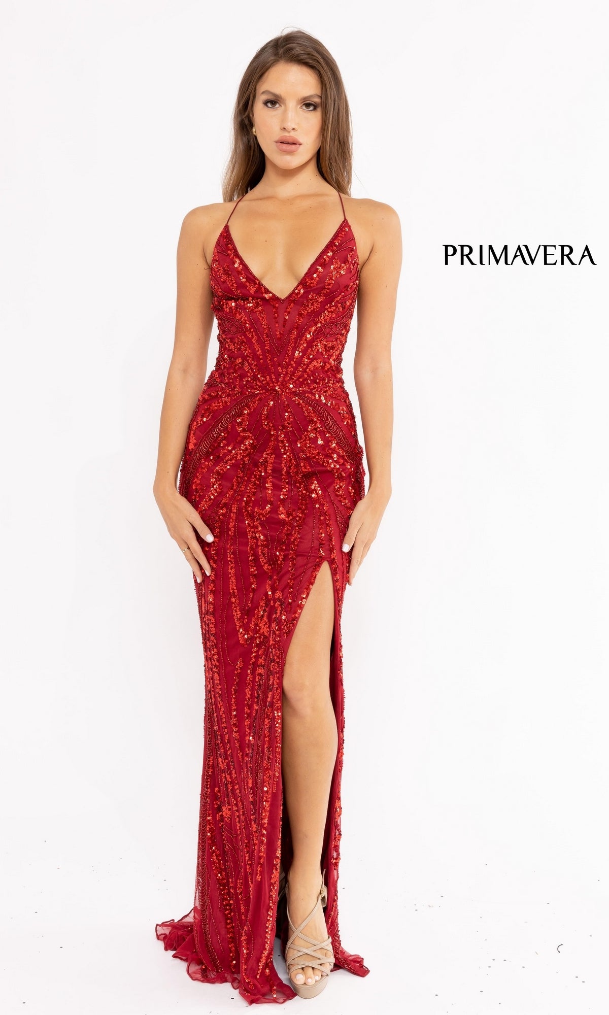 A woman faces forward wearing the Strappy-Back Long Sequin Prom Dress 3958—red, beaded, floor-length with a thigh-high slit and strappy heels.