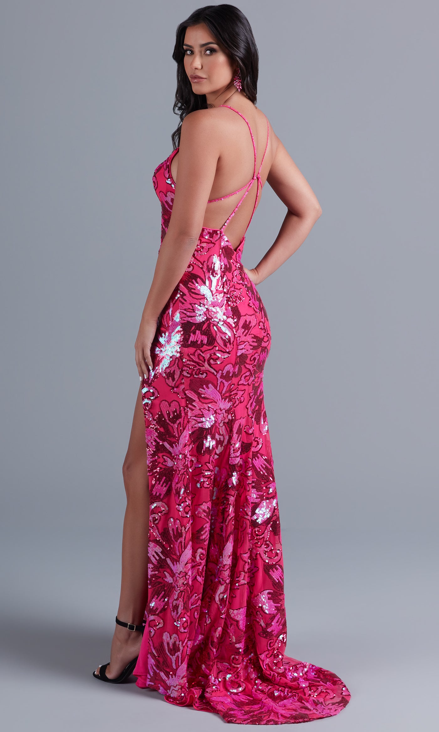 Model wears the Long Bright Sequin Unique Prom Dress RX5024—pink, backless with thin crisscross straps, side slit, and floral design—standing against a plain gray background.