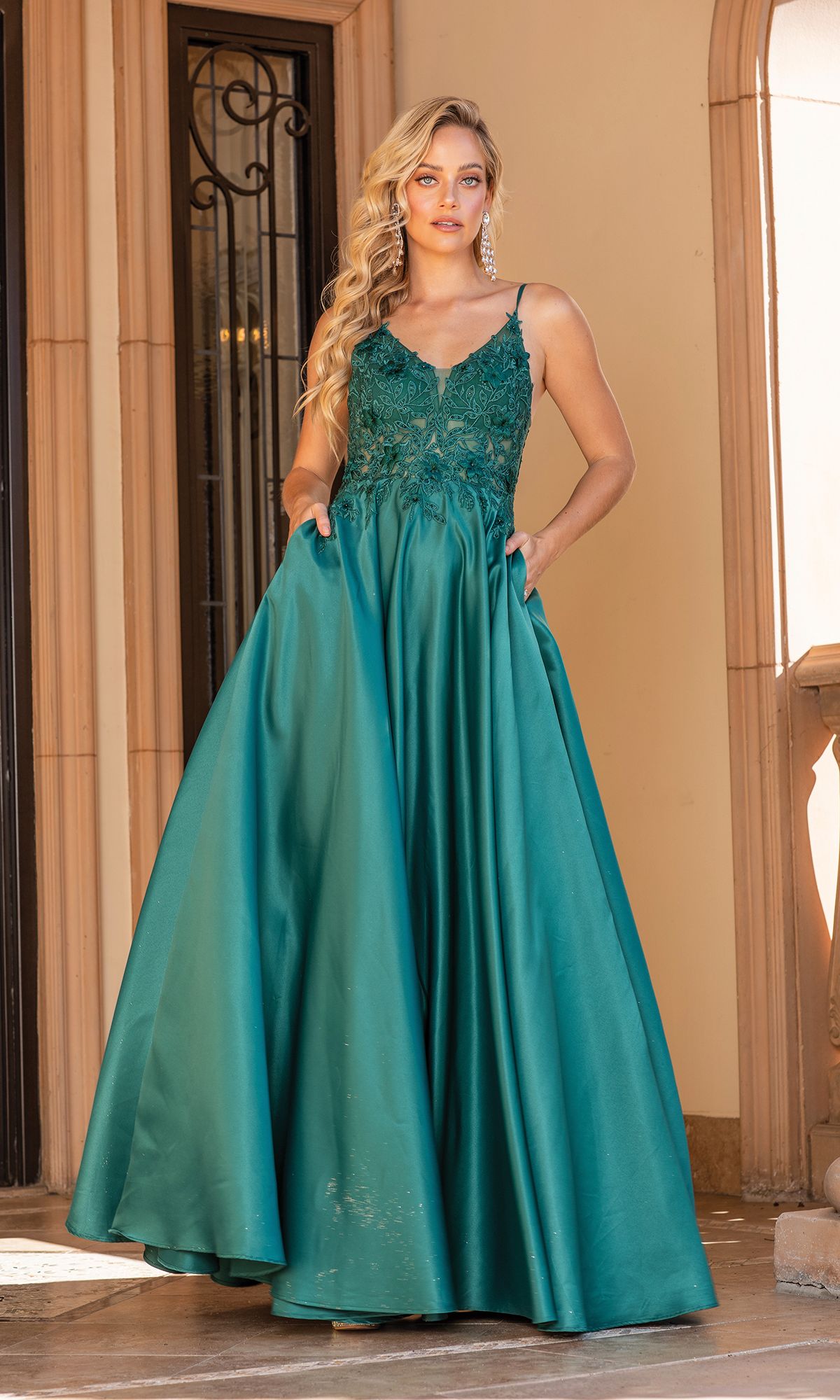 A woman stands in front of a doorway, radiating elegance in the A-Line Long Prom Ball Gown: Dancing Queen 4326, featuring a lace bodice and spaghetti straps—perfect for making a statement at any formal event.