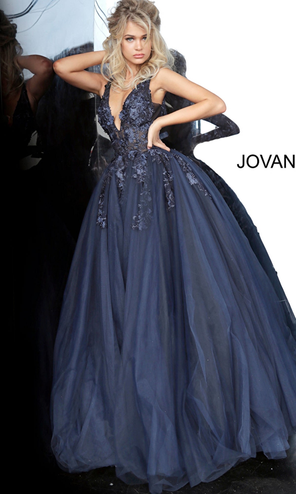 Woman in a deep blue Jovani Tulle Prom Ball Gown with a fitted V-neck bodice, floral appliques, and a full tulle skirt.