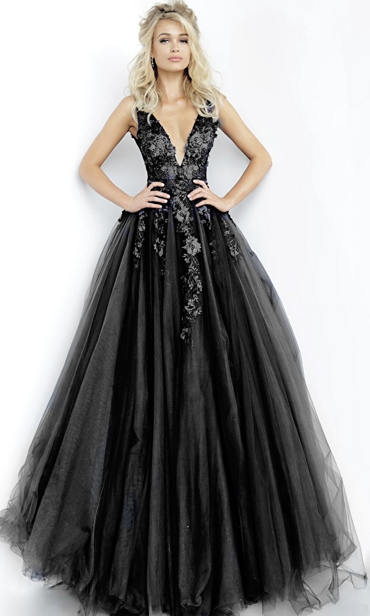 A woman stands against a white background wearing the Jovani Tulle Prom Ball Gown, featuring a sleeveless design, floor-length skirt, deep V-neckline, and delicate floral appliques on the lace bodice and skirt.