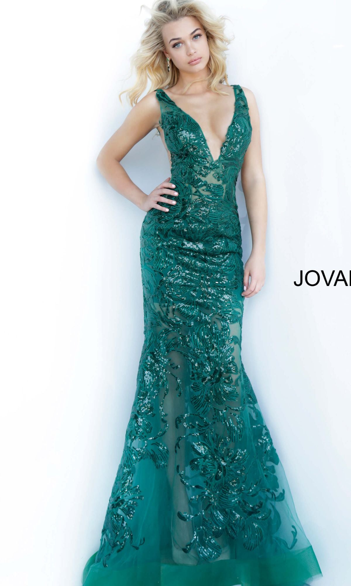 A woman poses in a sleeveless, floor-length green Jovani Embroidered Long Prom Dress with Sequins, featuring a deep V-neckline and beautiful sequin floral embroidery.