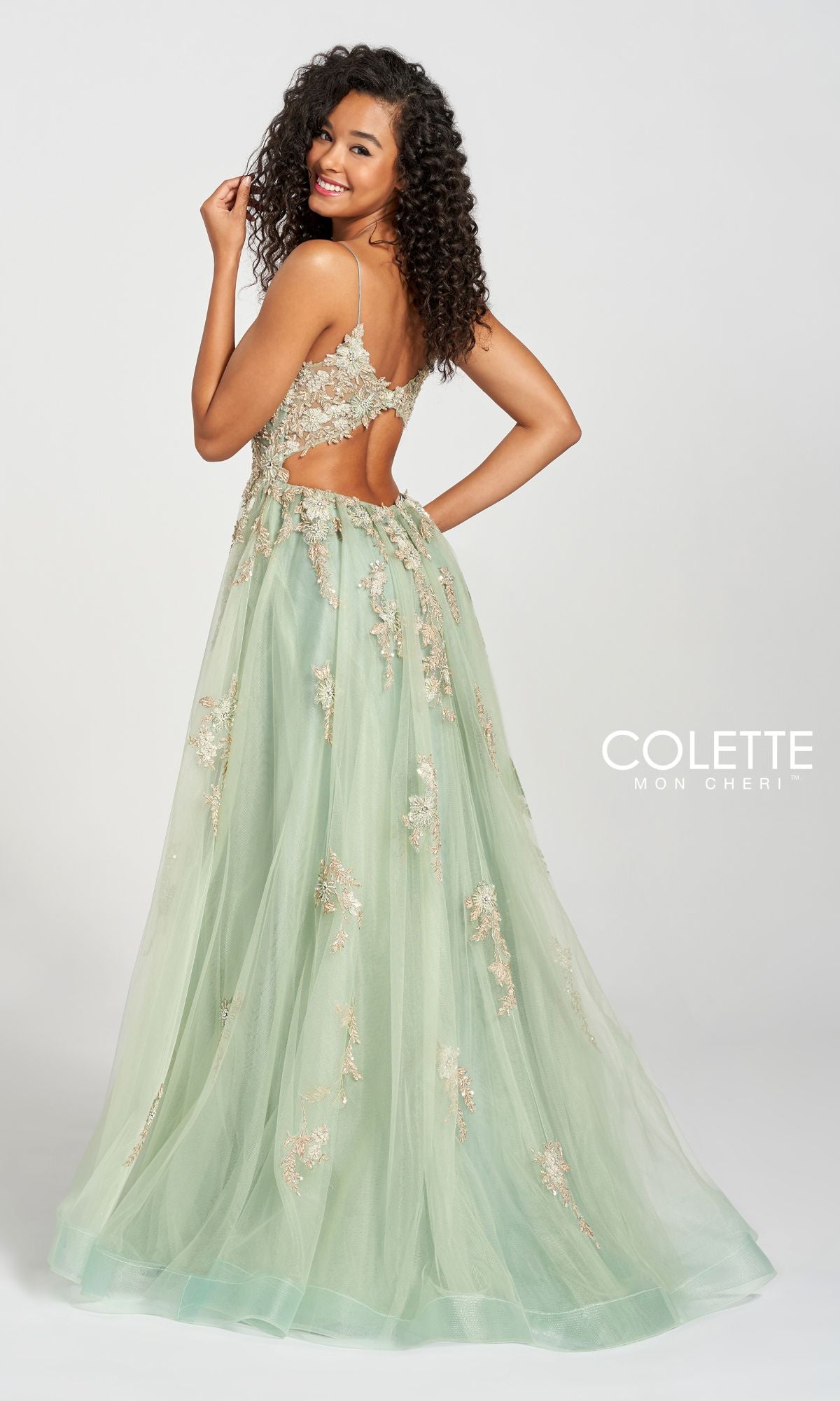 A woman poses in the Ivy Green A-Line Prom Ball Gown CL12207, featuring floral embellishments, a cut-out back, and a tulle skirt, standing against a plain white background.