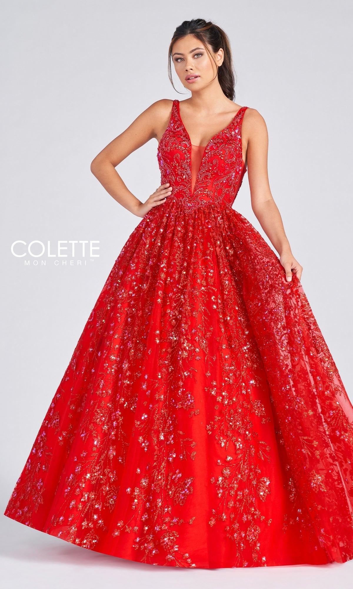 A woman poses in the Colette Designer Prom Sequin & Glitter Ball Gown, a sleeveless deep V-neck red ball gown with gold and red embroidery, radiating designer elegance against a plain light background.