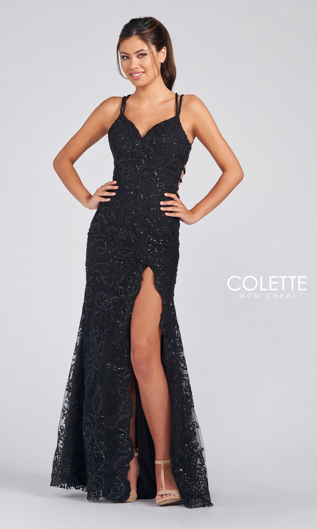 A woman wears the Colette by Daphne Prom Dress CL12280, a sleeveless black lace and sequin gown with thin straps, a thigh-high slit, and intricate detailing, standing against a plain background.