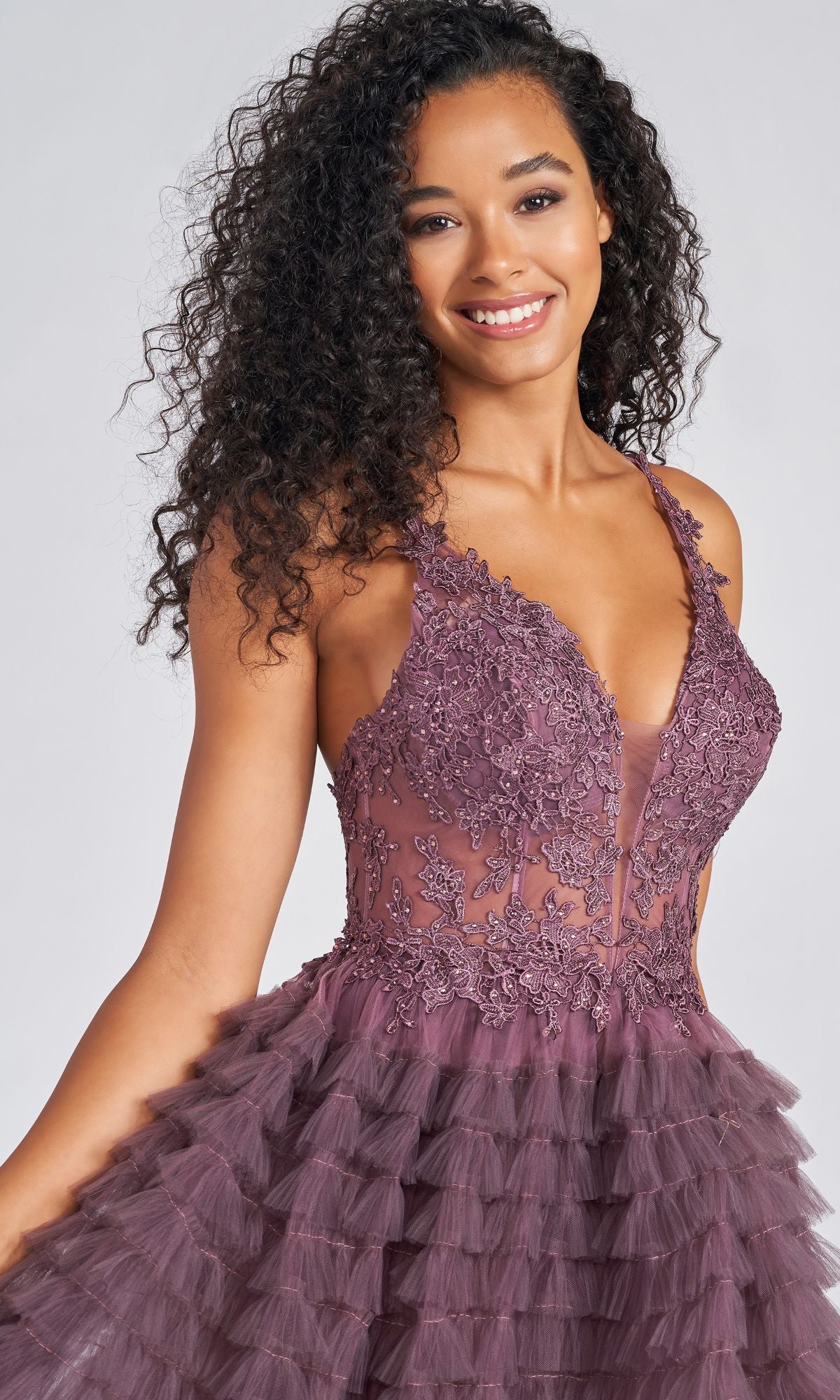 A woman in the High-Low Tiered-Tulle Prom Dress CL12281, featuring a sleeveless deep v-neck, lace bodice, and layered mauve tulle skirt, smiles at the camera.