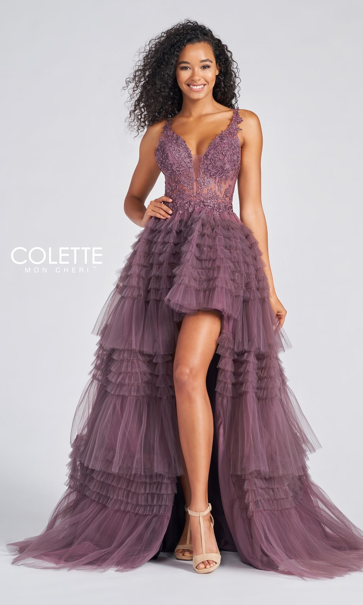 A woman models the High-Low Tiered-Tulle Prom Dress CL12281, featuring a sleeveless deep-plum design with a lace bodice and tiered tulle skirt, set against a plain background.