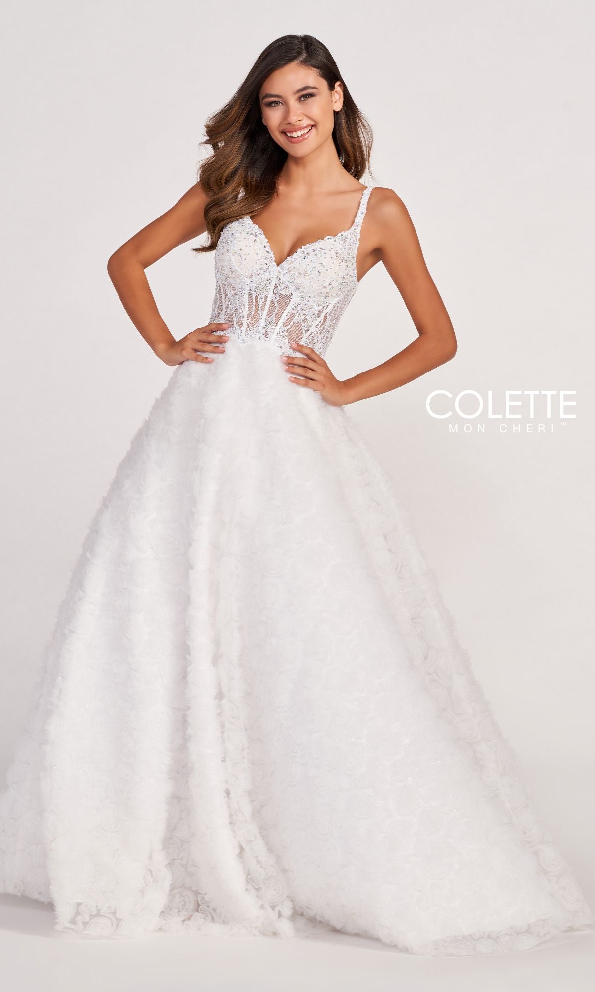 A woman smiles against a plain background wearing the Colette Sheer-Bodice Rosette Beaded Lace Ball Gown, a sleeveless white evening dress with sheer panels and a full, textured skirt—perfect for prom.