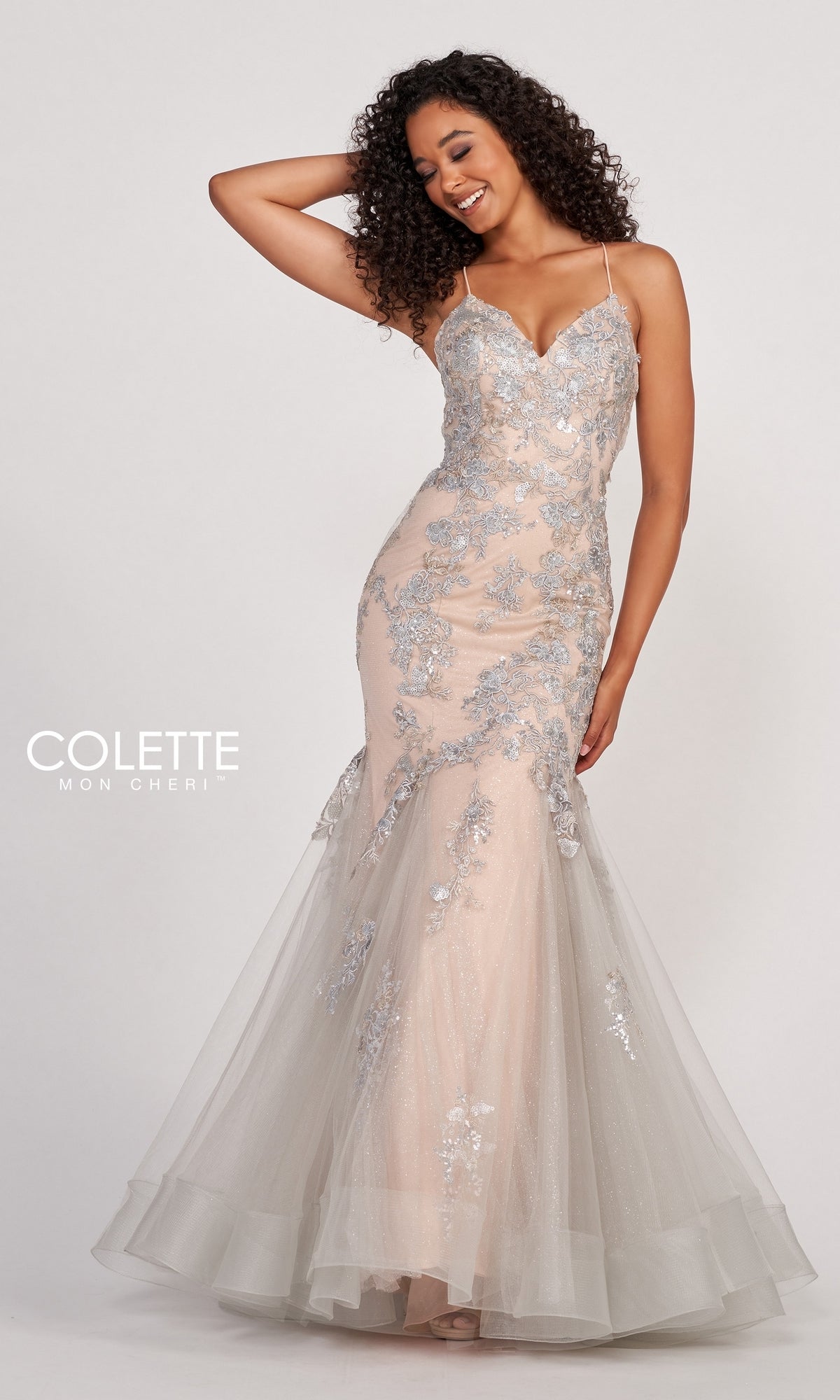 A woman poses with one hand on her head in the Colette Silver Lace Long Nude Mermaid Prom Dress, featuring a fitted, floor-length silhouette with floral lace details and spaghetti straps.