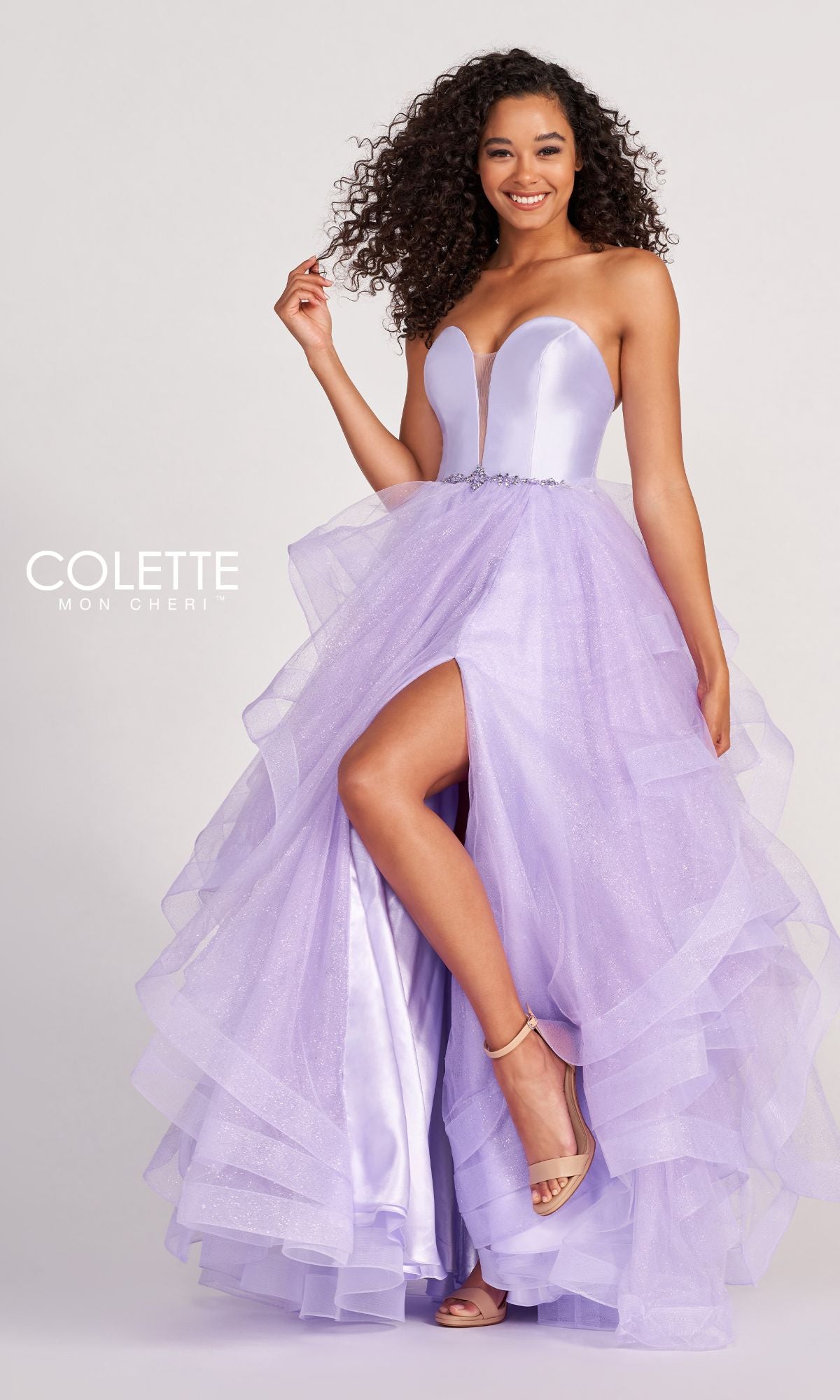 A woman stands and smiles against a plain background, wearing the Colette Glitter-Tulle Layered Long Prom Ball Gown—strapless, lavender, with a high slit and layered skirt.