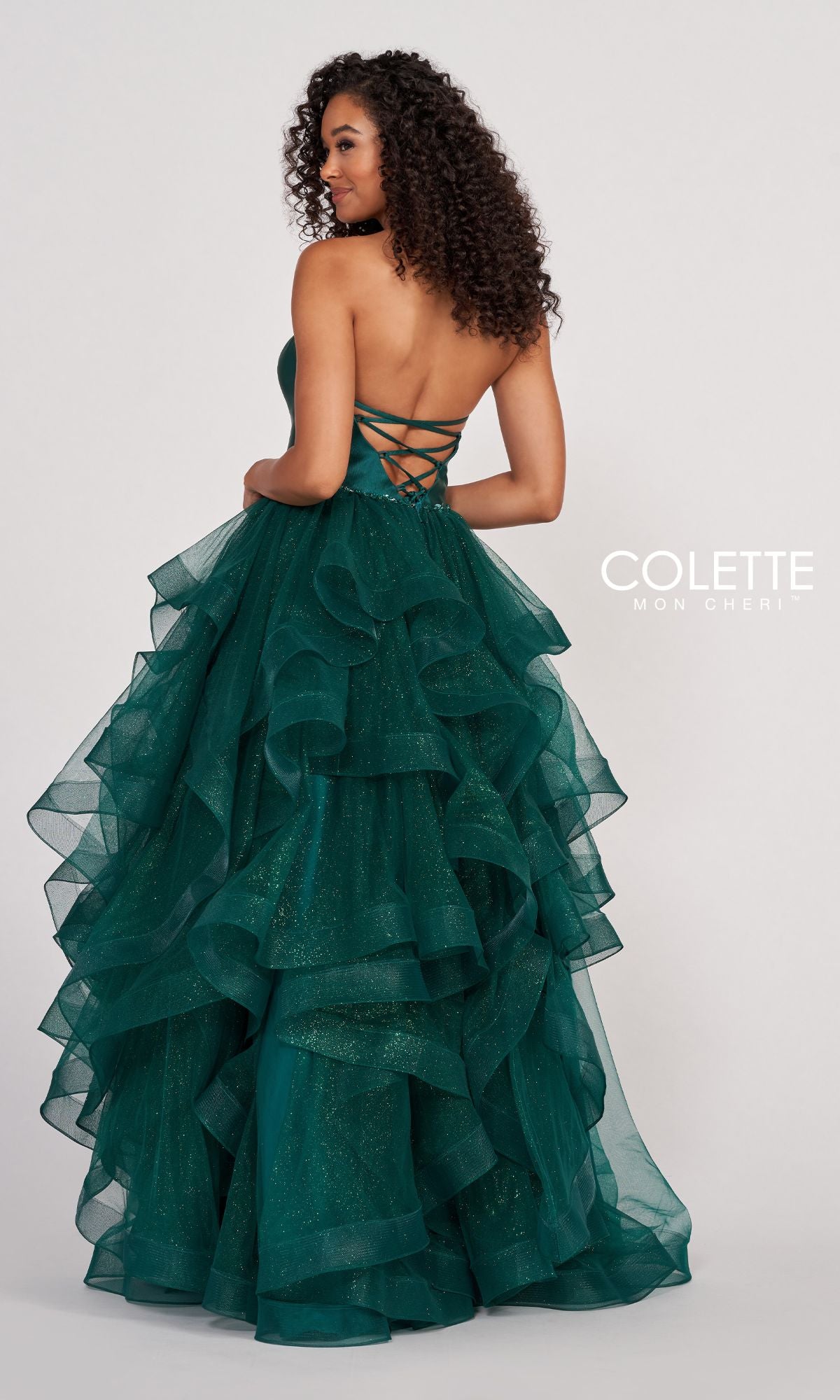 A woman in a strapless formal dress faces away, wearing the Colette Glitter-Tulle Layered Long Prom Ball Gown—its green tulle layers, lace-up back, and subtle glitter sparkle for a stunning effect.