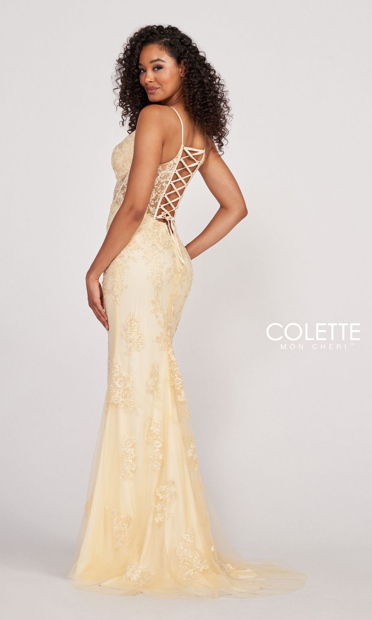 Woman in a fitted, light yellow Colette Beaded-Lace Long Prom Dress with corset back stands sideways, looking at the camera.