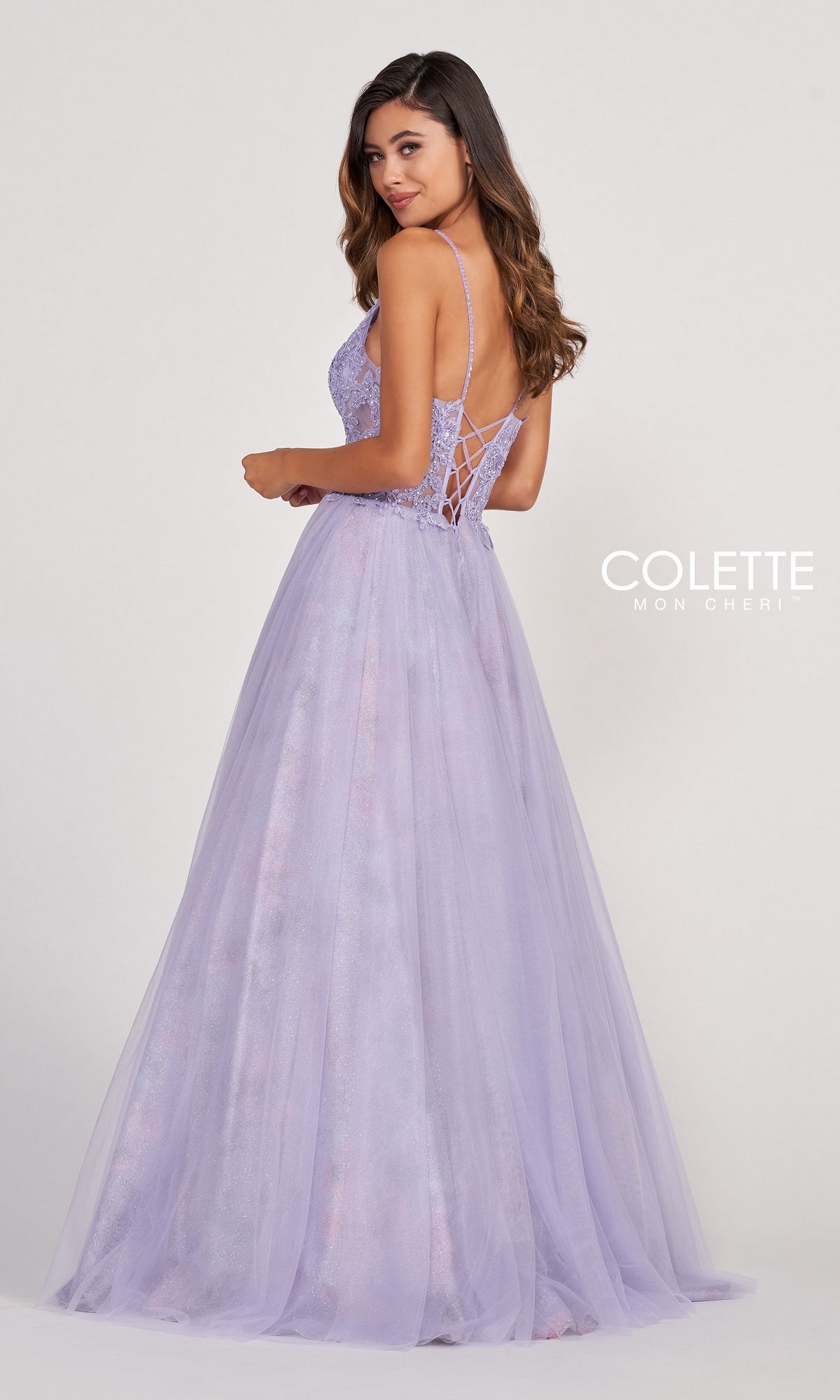A woman wearing the Pastel Long Tulle Prom Ball Gown by Colette, featuring a lace-up back, thin straps, and a full skirt, stands facing slightly away from the camera.