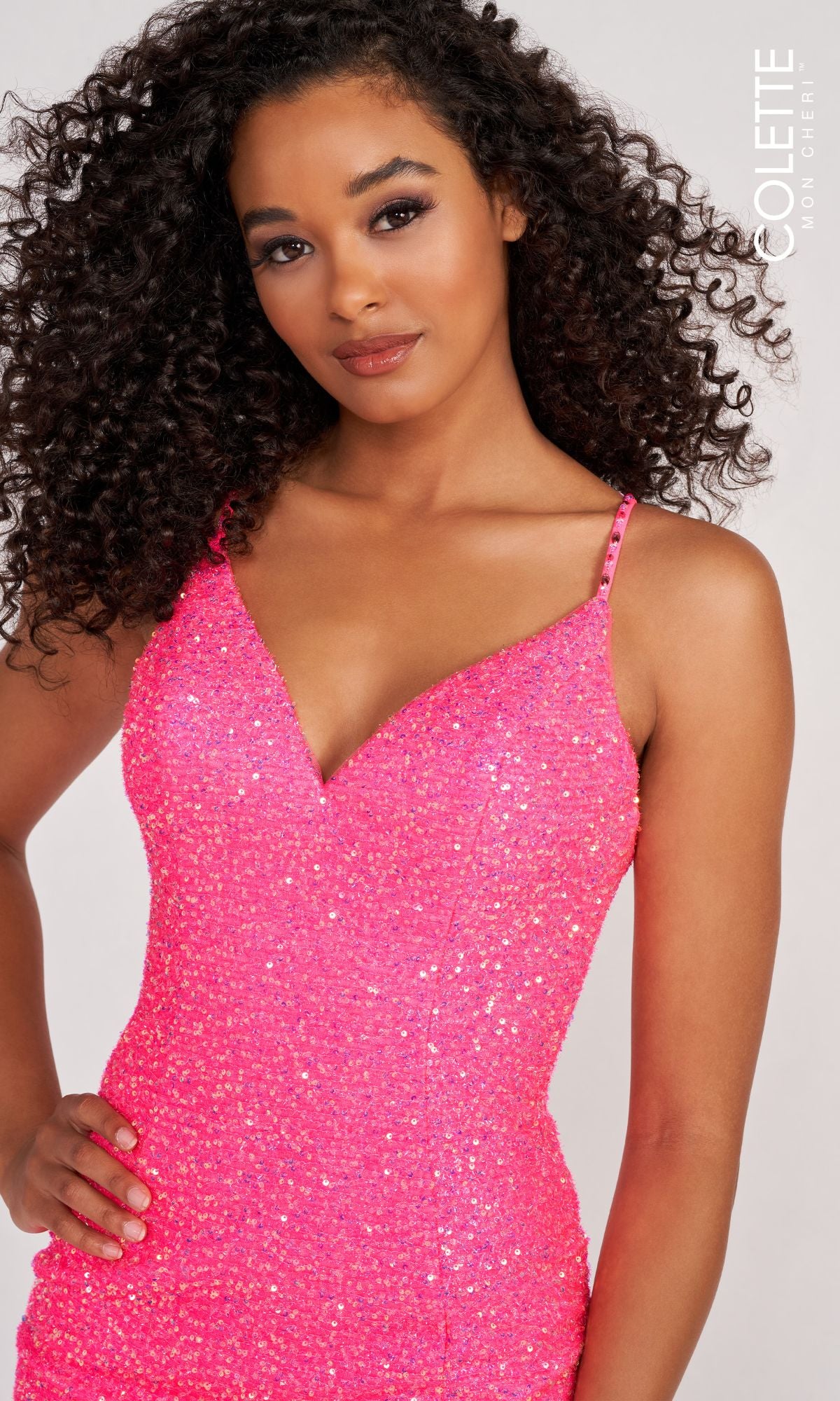 Woman with curly hair wears the Colette CL2012 Stretch-Sequin Open-Back Prom Dress in bright pink, standing with one hand on her hip against a light background.
