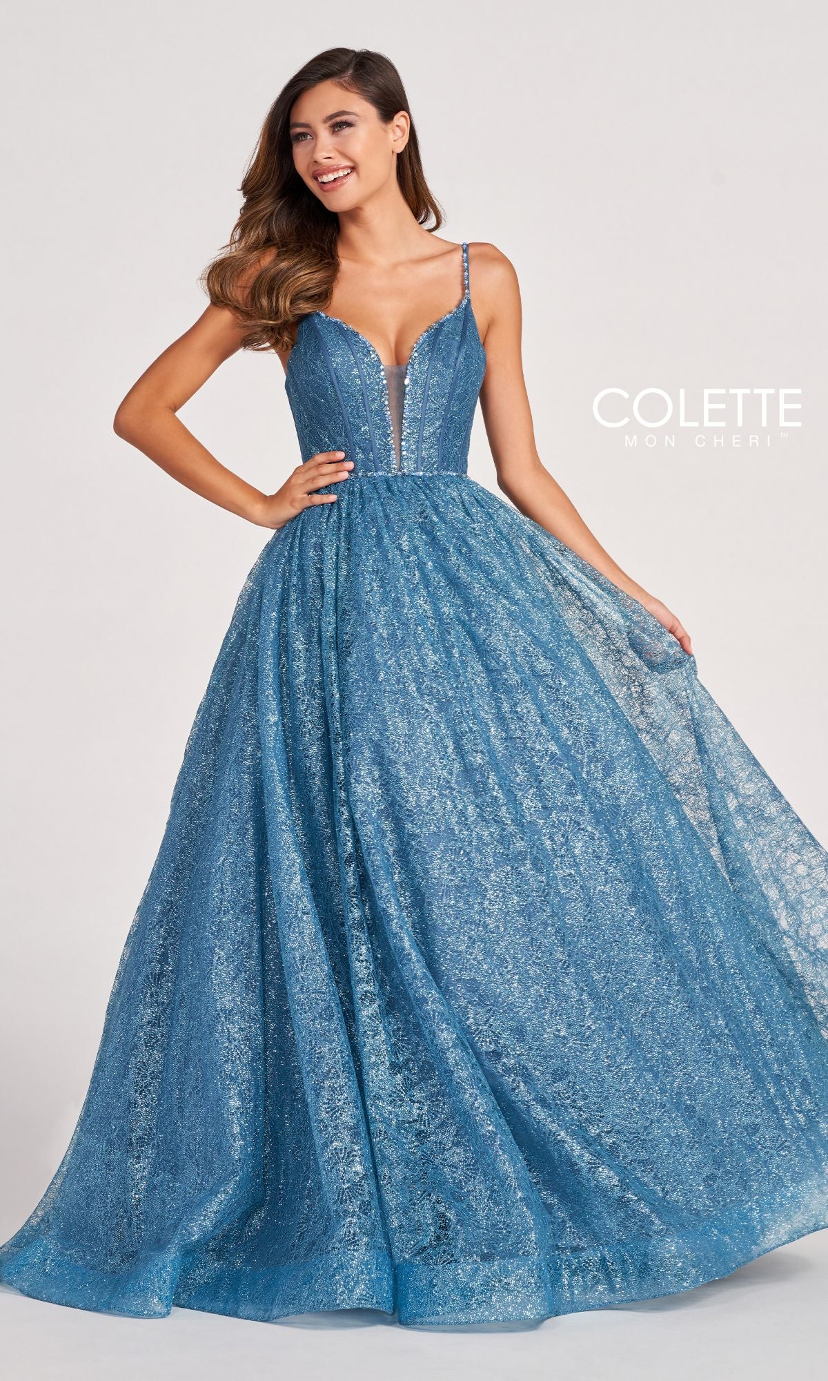 A woman wearing the Colette CL2018 Deep V-Neck Glitter-Lace Ball Gown, with a fitted bodice, thin straps, and full skirt, stands against a plain background.