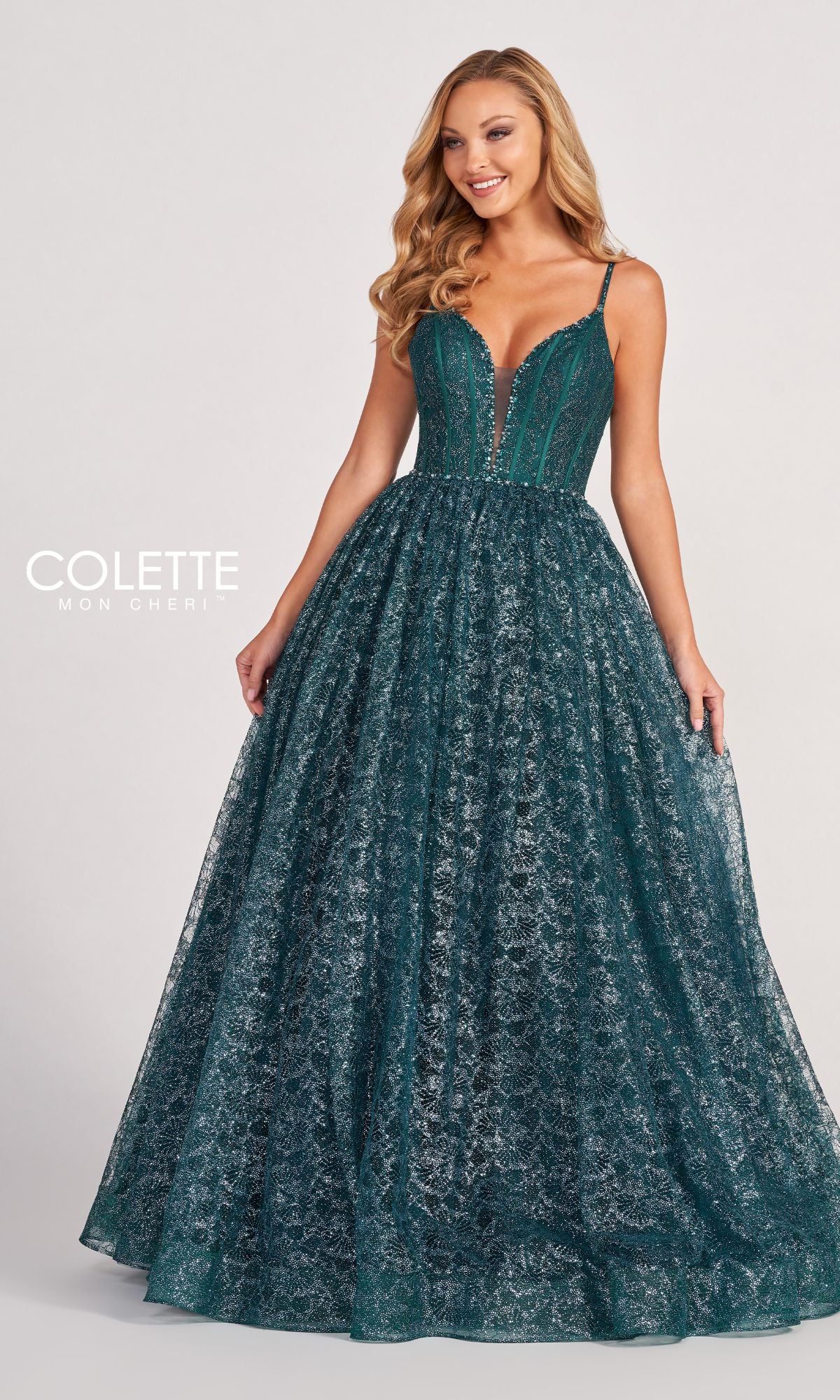 A woman poses against a plain background in the Colette CL2018 Deep V-Neck Glitter-Lace Ball Gown, a sleeveless deep green evening dress with a fitted bodice and a full, sparkling skirt.