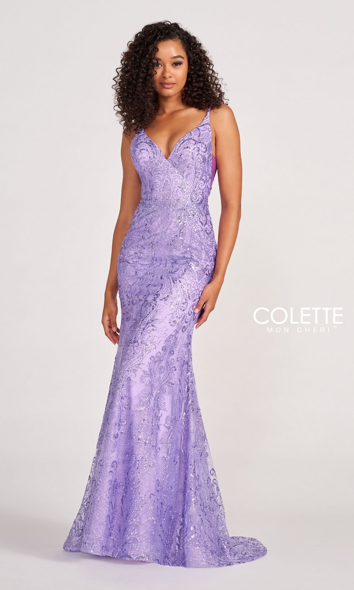 A woman stands before a plain background in the Colette CL2019 Long Prom Dress in Glitter-Sequin, a sleeveless, floor-length lavender gown with a fitted bodice, flared skirt, subtle pattern, and elegant V-neckline.