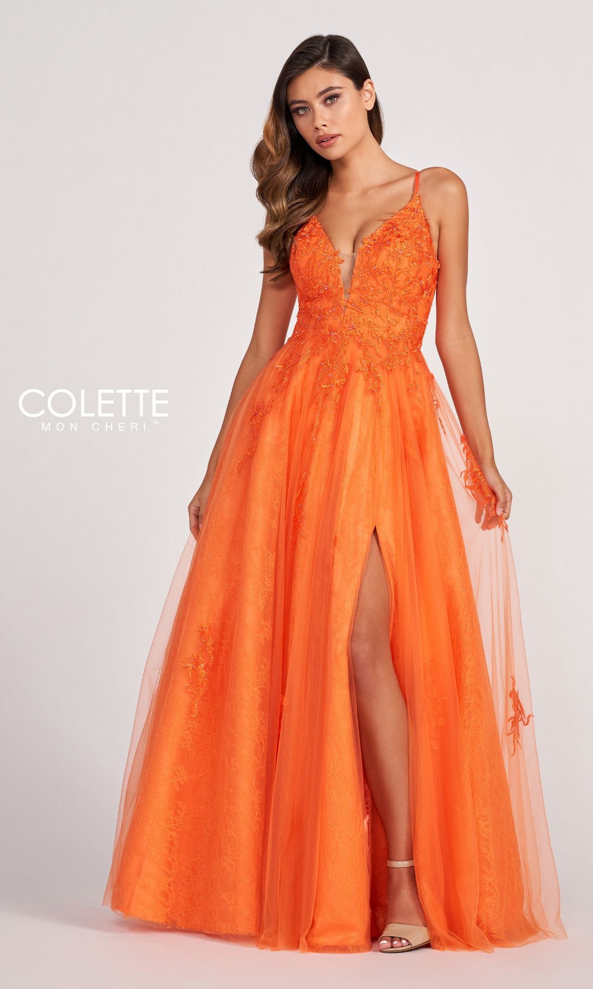 A woman wears the Beaded Lace Long A-Line Prom Dress Colette CL2025, featuring a bright orange hue, sleeveless design, deep V-neckline, beaded lace floral details, and a high slit.