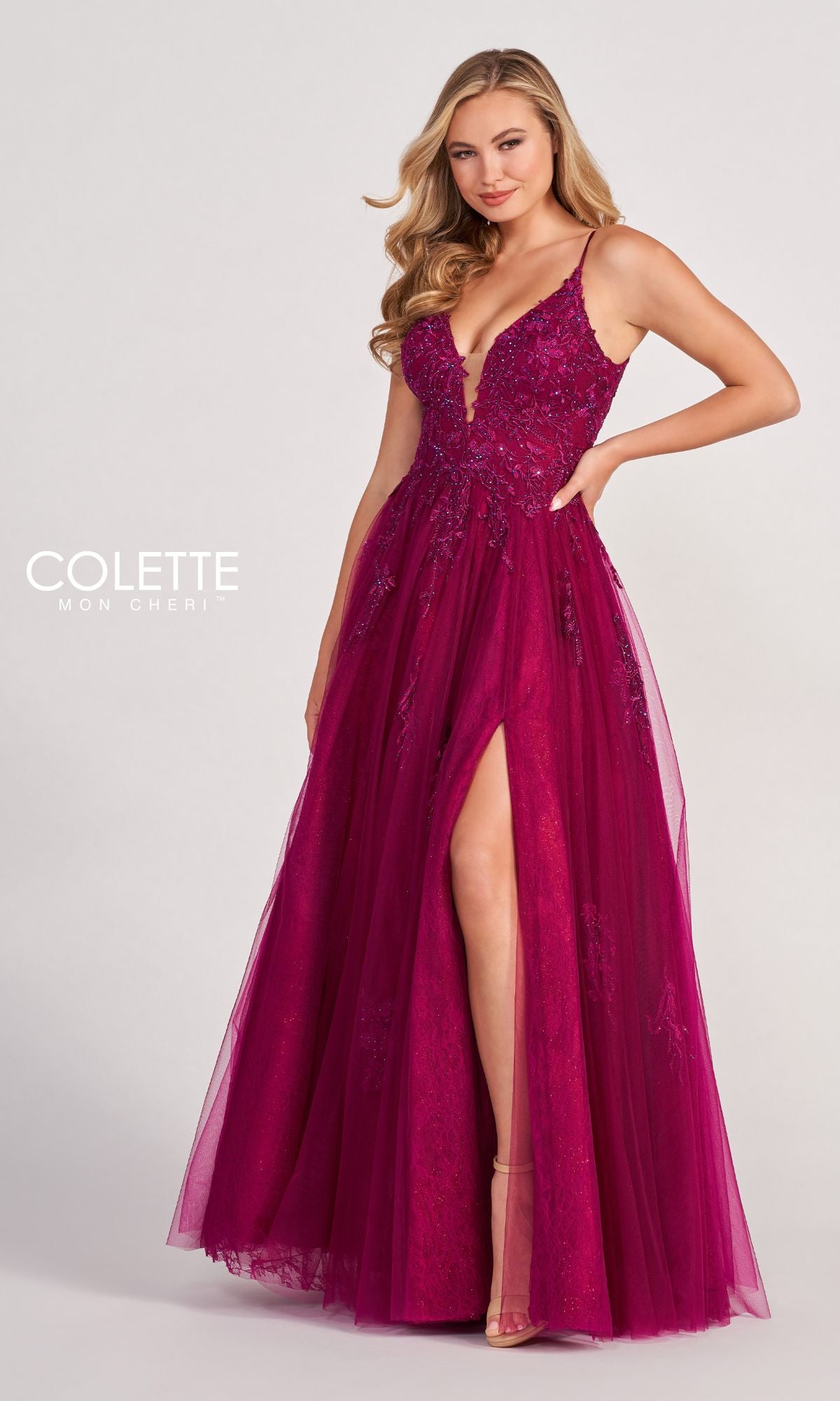 A woman poses against a plain background wearing the Beaded Lace Long A-Line Prom Dress Colette CL2025, featuring a sleeveless deep magenta design with a plunging neckline, beaded lace details, and a thigh-high slit.