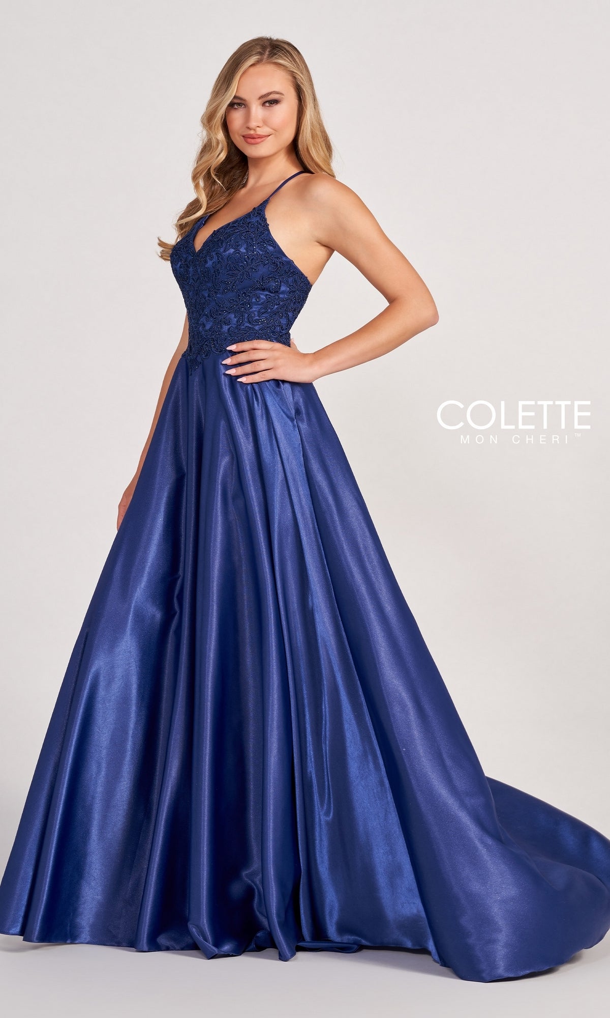 A woman stands against a plain background wearing the Colette by Daphne Satin Prom Ball Gown CL2033, featuring a floor-length royal blue satin skirt, fitted lace bodice, and spaghetti straps.