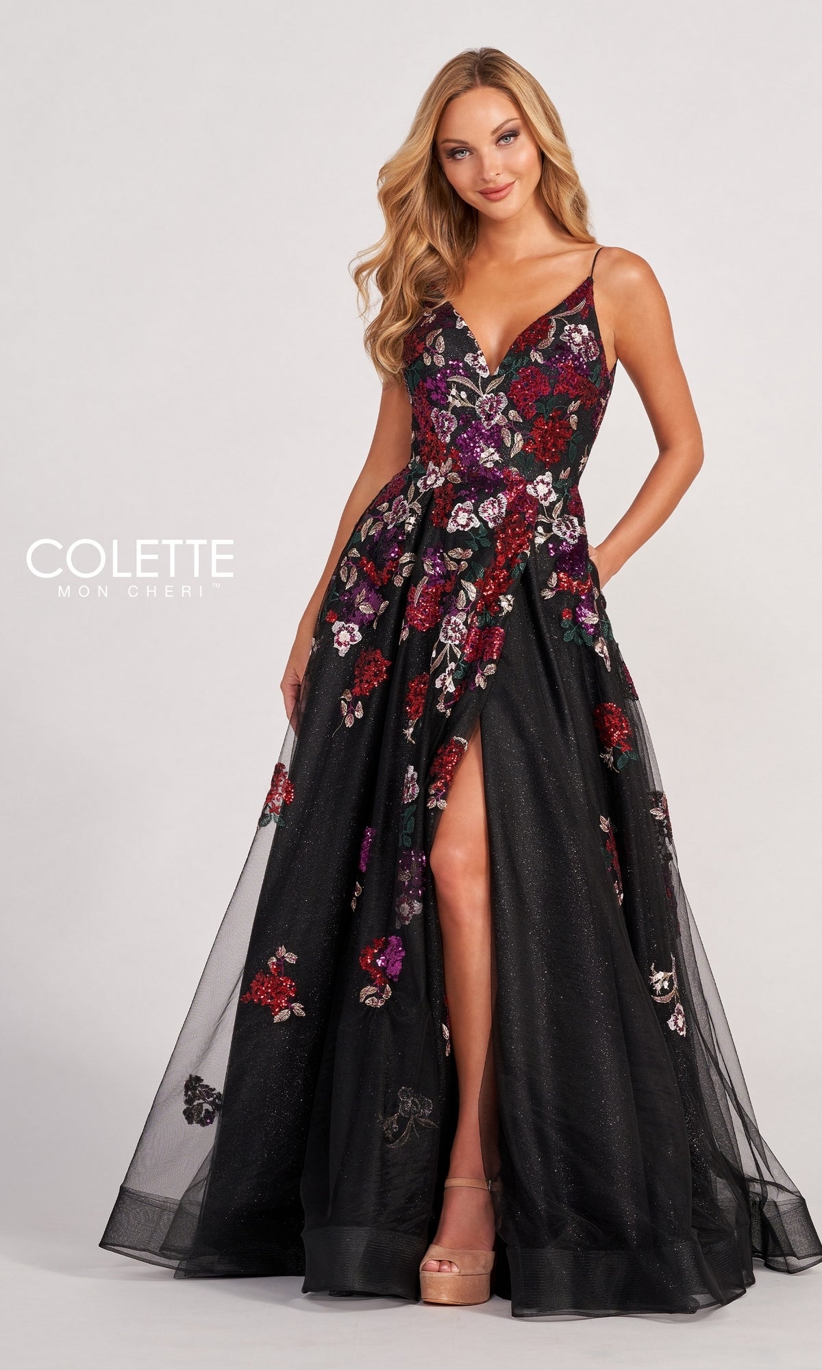 A woman models the Black Prom Dress CL2069, featuring multicolor floral appliques, a deep V-neckline, thin straps, and a high slit, standing against a plain background.