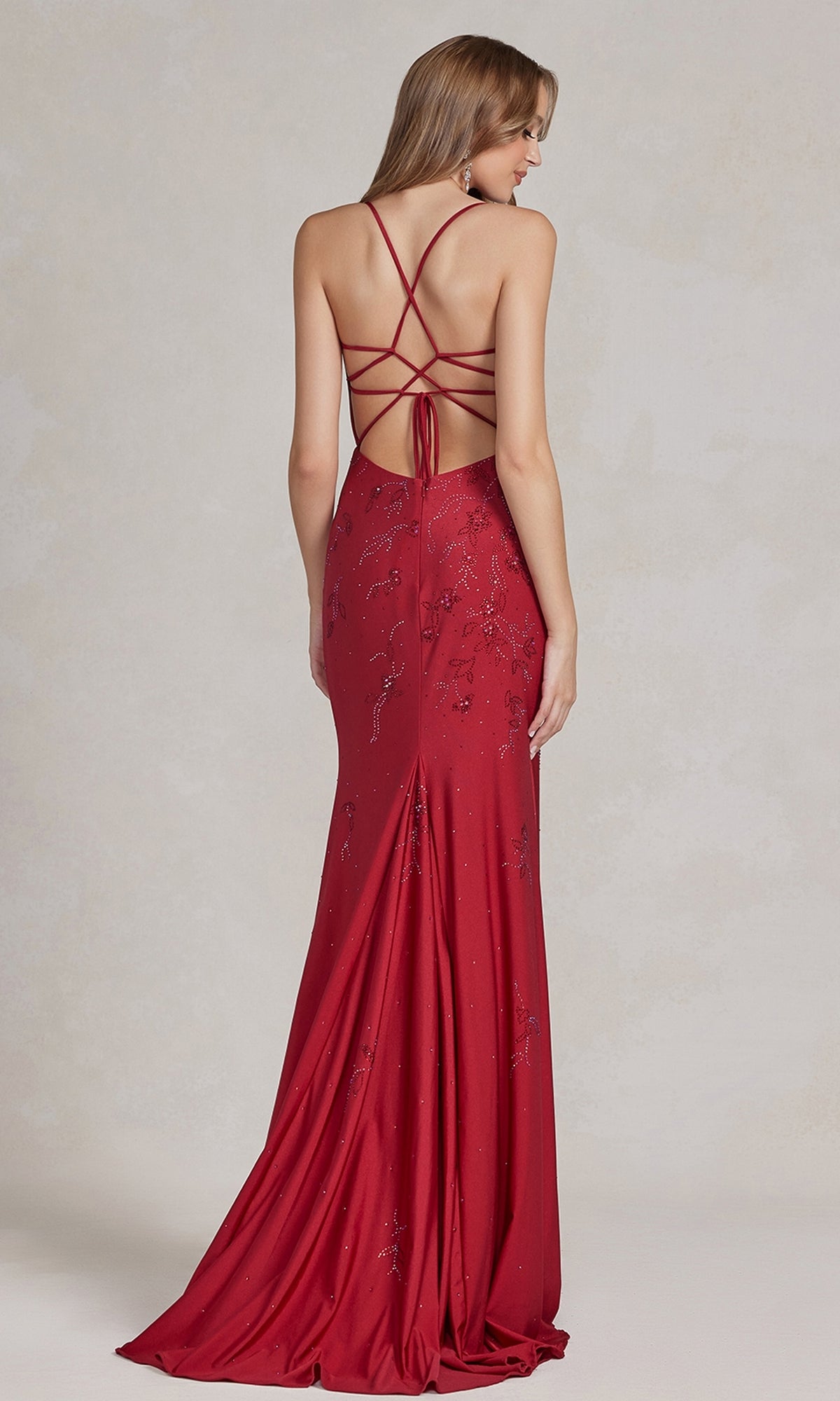 A woman stands against a neutral background, wearing the Backless Prom Dress with Floral Beaded Pattern—floor-length, fitted silhouette, v-neckline, sequin floral beading, and an open strappy back.