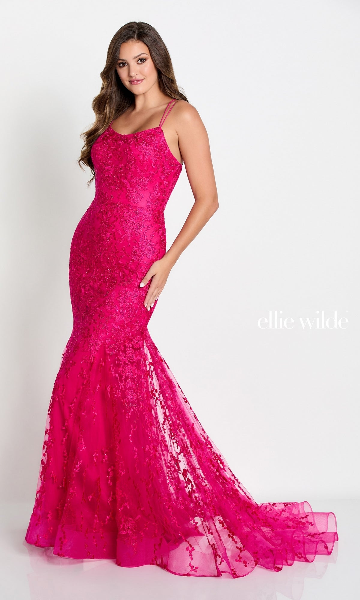 A woman poses in the Long Lace Mermaid Prom Dress with a fitted bright pink design, thin straps, floral lace detailing, a small train, and an elegant strappy open back.
