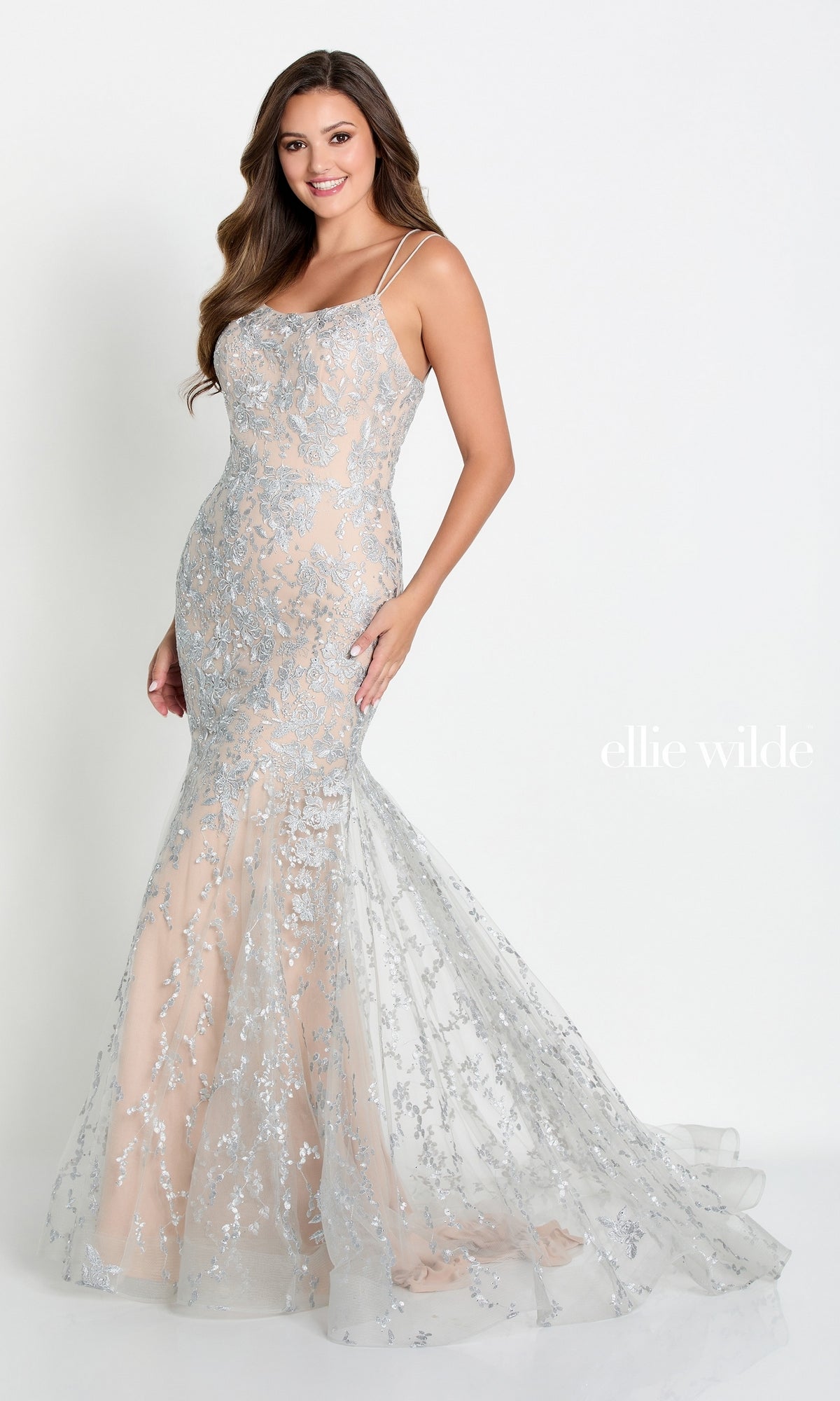 A woman wears the Long Lace Mermaid Prom Dress with Strappy Back, featuring silver floral-embroidered lace and thin straps. She stands against a plain white background, showing off the elegant open-back design.