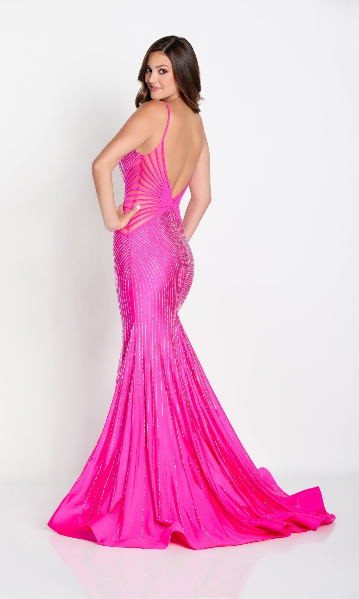 A woman poses with her back slightly turned and smiles in the Ellie Wilde Stripe Sheer-Side Prom Dress EW34004, a bright pink gown featuring thin straps and shimmering vertical lines.