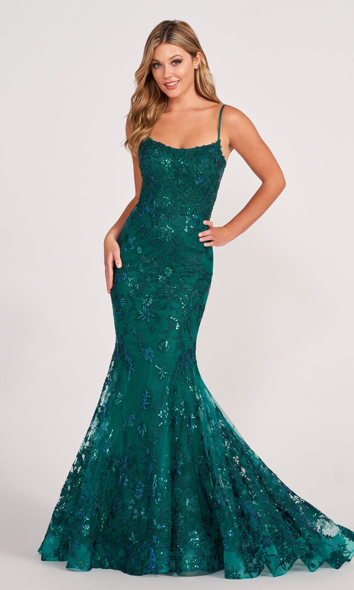 A woman models the Ellie Wilde Embroidered-Lace Mermaid Prom Dress, a sleeveless, fitted emerald gown with intricate lace detailing and a dramatic mermaid silhouette against a plain background.