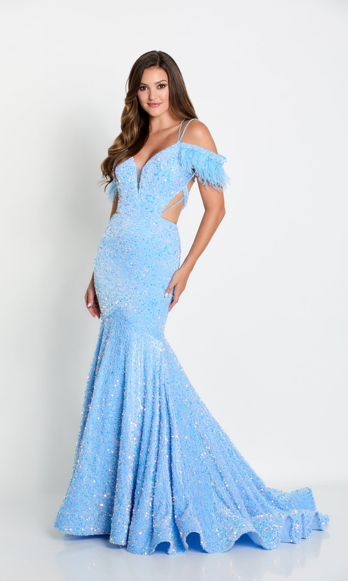 A woman stands against a plain white background wearing the Long Sequin Cut-Out Prom Dress with Feathers, a shimmering light blue gown featuring feathered off-the-shoulder sleeves.