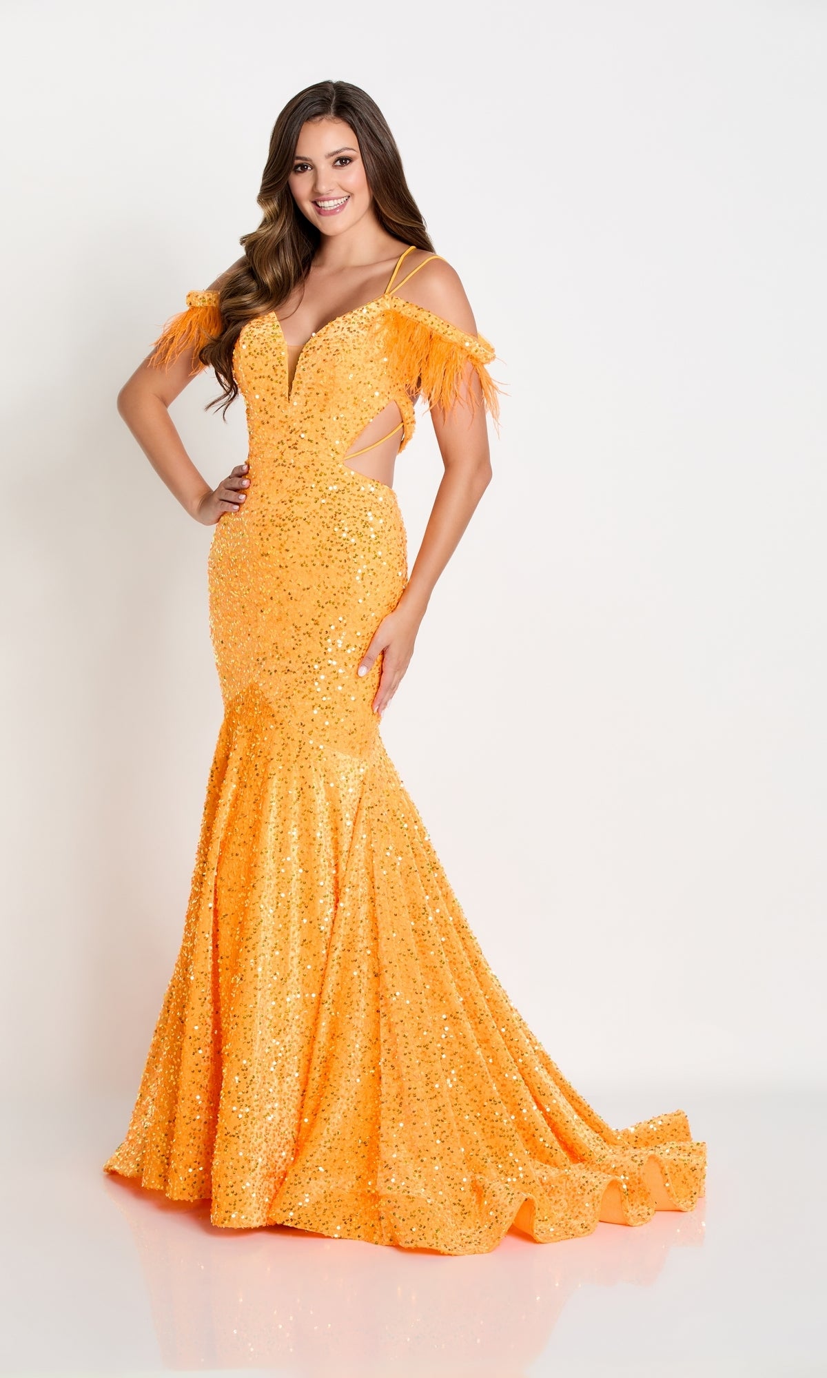 A woman models the Long Sequin Cut-Out Prom Dress with Feathers in bright orange, featuring sequin details and feathered shoulder accents, against a white background.