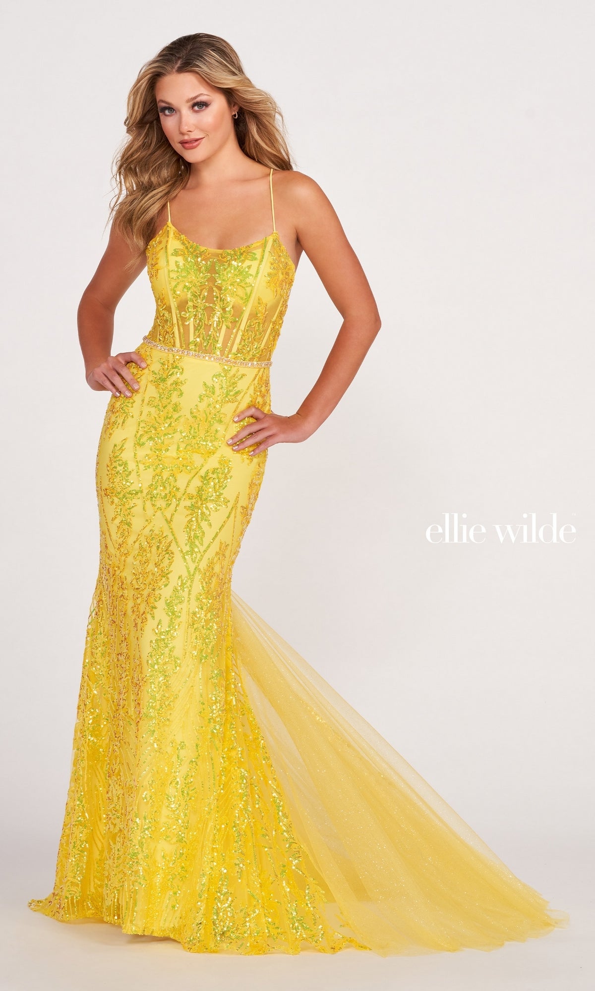 A woman poses in a fitted, yellow Sheer-Corset Long Sequin Mermaid Prom Dress with floral embroidery and thin straps. This open-back formal gown features sheer detailing and a flared tulle hem.