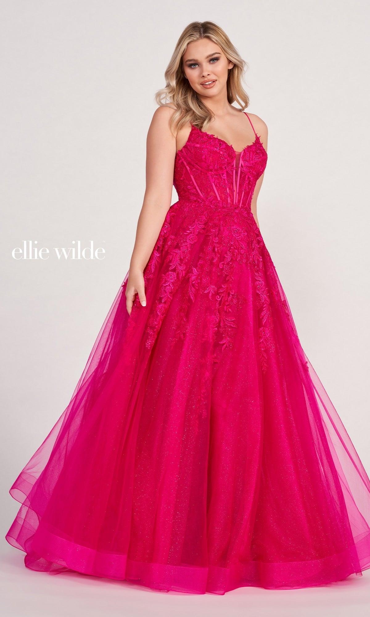 A woman models the Sheer-Corset Long Lace Prom Ball Gown EW34036 in vibrant pink lace with floral details and a sheer overlay, standing before a plain light background.