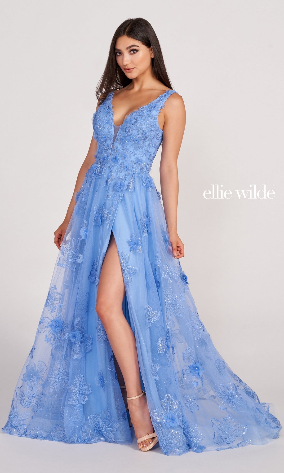 A woman models the Ellie Wilde Faux-Wrap Embroidered-Lace Prom Dress in light blue, featuring a sleeveless design, deep V neckline, high front slit, floral appliqué, and lace embroidery. The text