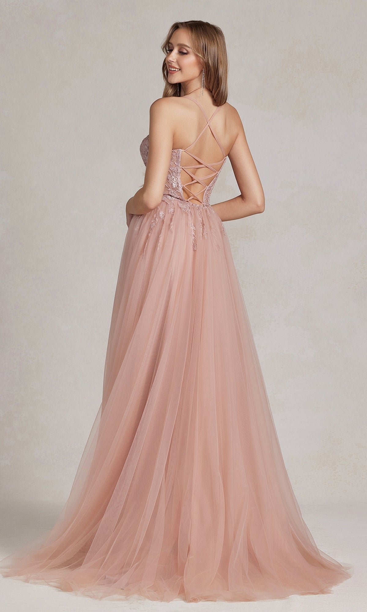 A woman models the Corset-Bodice Long Pastel Prom Dress, featuring a floor-length blush tulle skirt and lace-up back, as she stands looking over her shoulder.