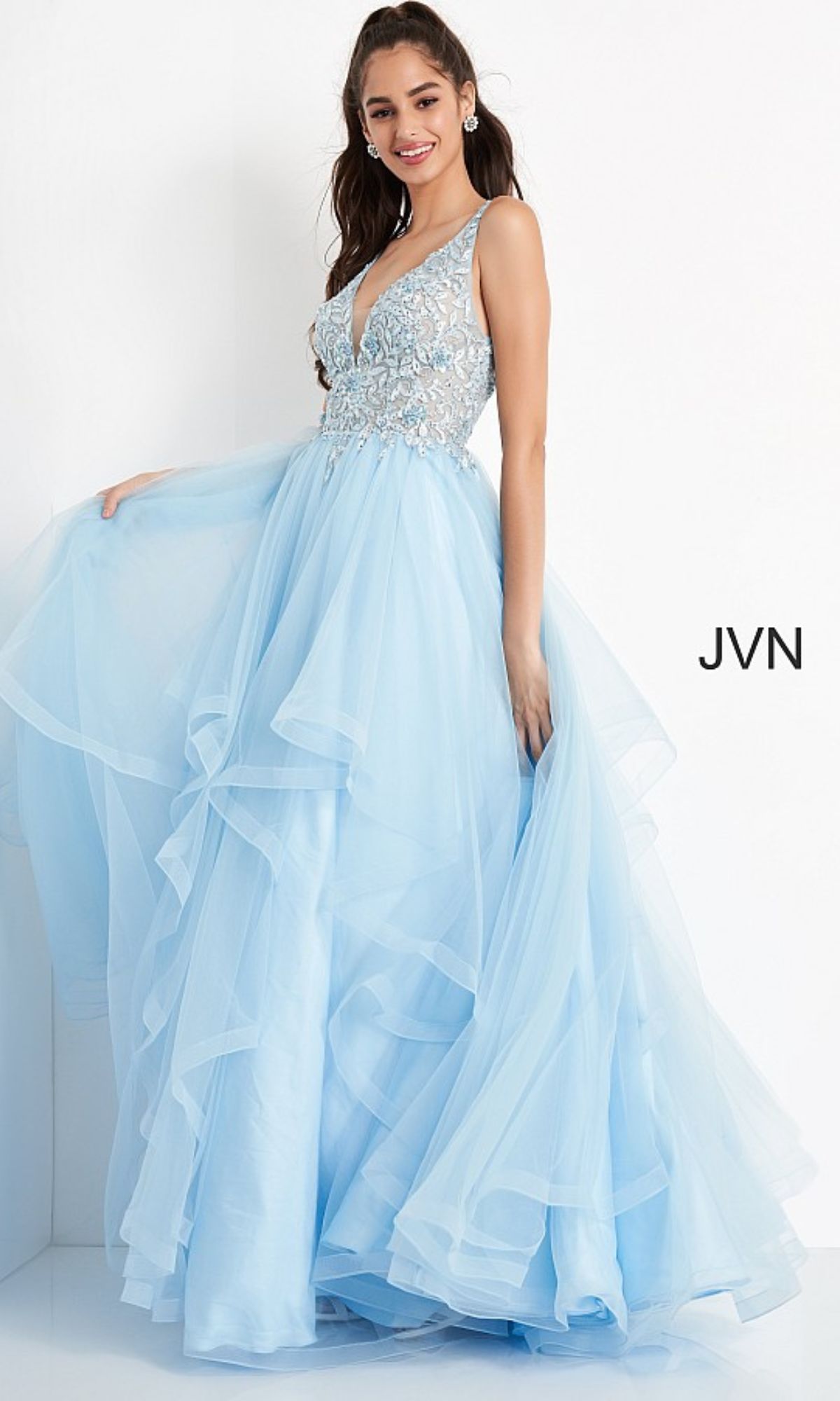A woman stands against a white background wearing the Jovani Prom Ball Gown with a layered tulle skirt and an embellished sleeveless bodice in light blue.