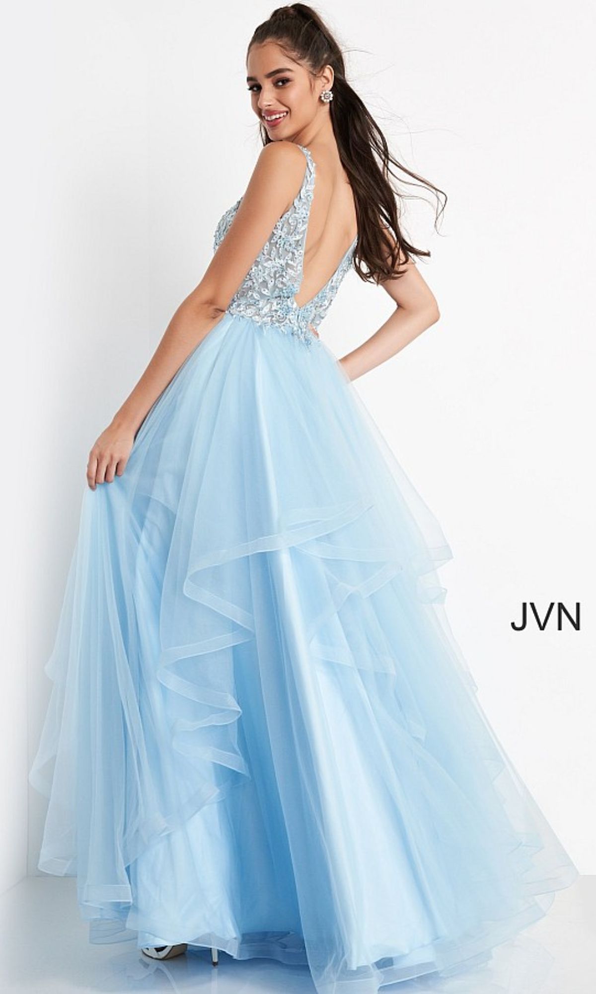 A woman poses in a Jovani Prom Ball Gown with Layered Skirt, featuring a light blue hue, tulle layers, and an embellished sleeveless bodice with a low back.