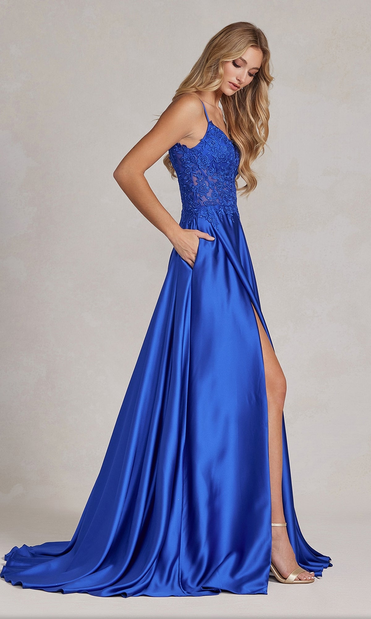 A woman wears the Faux-Wrap A-Line Long Prom Dress with Corset, featuring a royal blue satin skirt, beaded-lace bodice, thin straps, thigh-high slit, and pockets, standing against a neutral background.