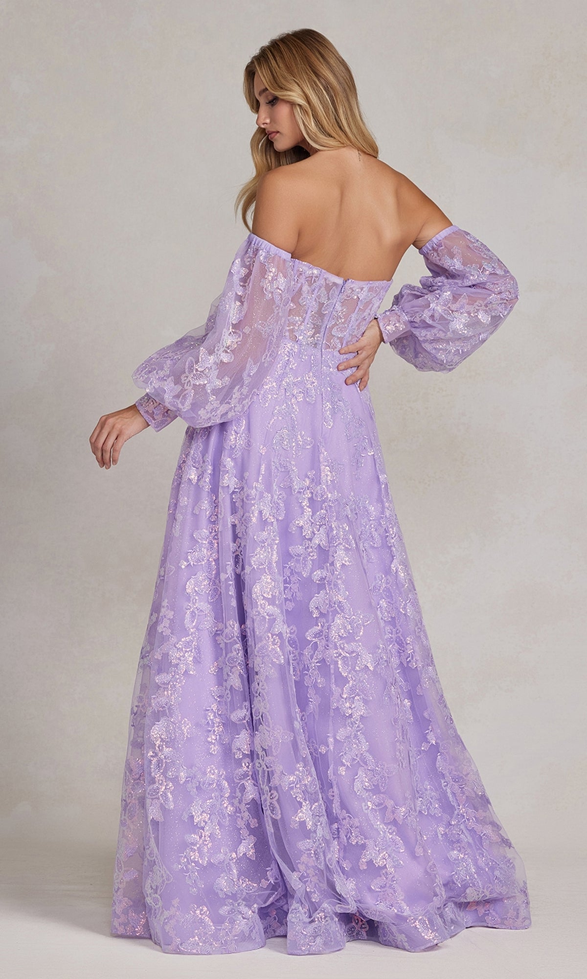 A woman models the Long Puff-Sleeve Prom Dress with Sheer Bodice—an off-the-shoulder, a-line gown in lavender lace with removable long sleeves and a floral pattern, standing with her back and head turned slightly to the side.