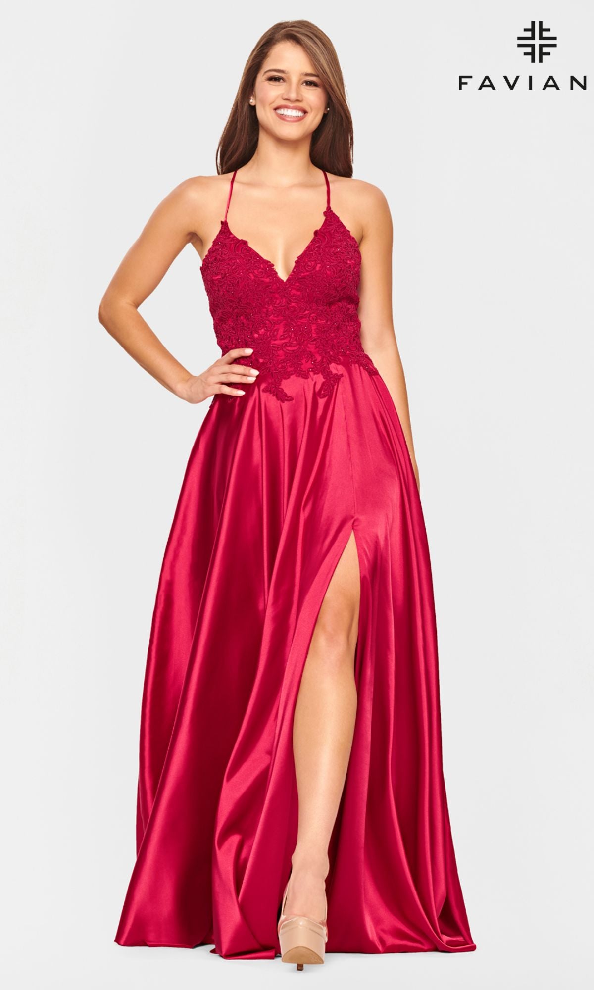 A woman stands smiling against a plain background in the Faviana Lace-Bodice Long A-Line Prom Dress, featuring a sleeveless deep red design, embroidered lace bodice, spaghetti straps, and a high slit.