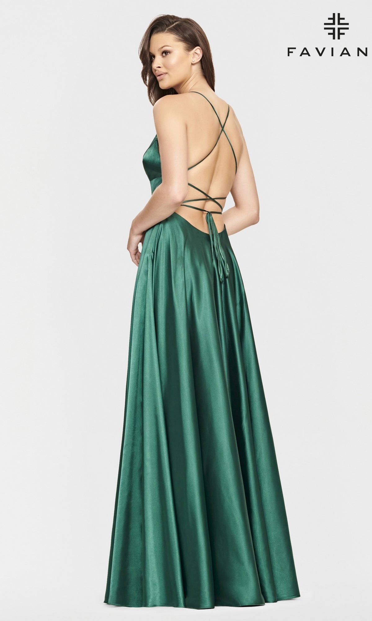 A woman models the Long Open-Back Formal Prom Dress by Faviana in emerald green satin, featuring thin straps and a crisscross open back, standing against a white background.